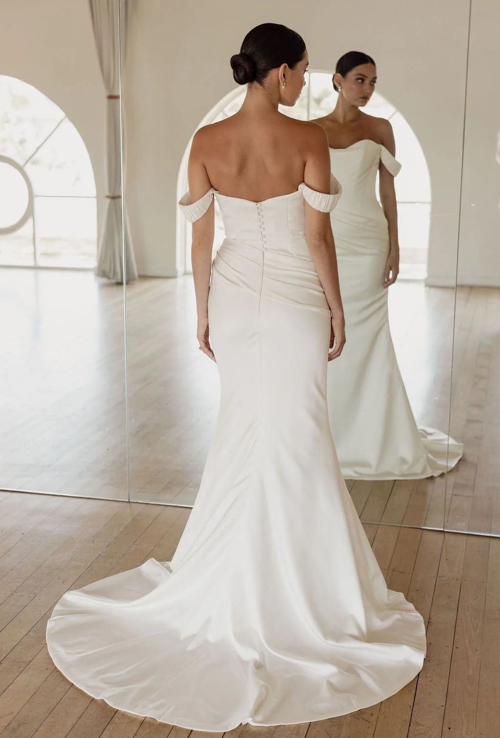 Demi by Trish Peng fitted satin crepe wedding dress featuring an asymmetric draped bodice, off-the-shoulder cowl neckline, removable straps and softly ruched skirt, available at Spellbound Bridal Ireland.
