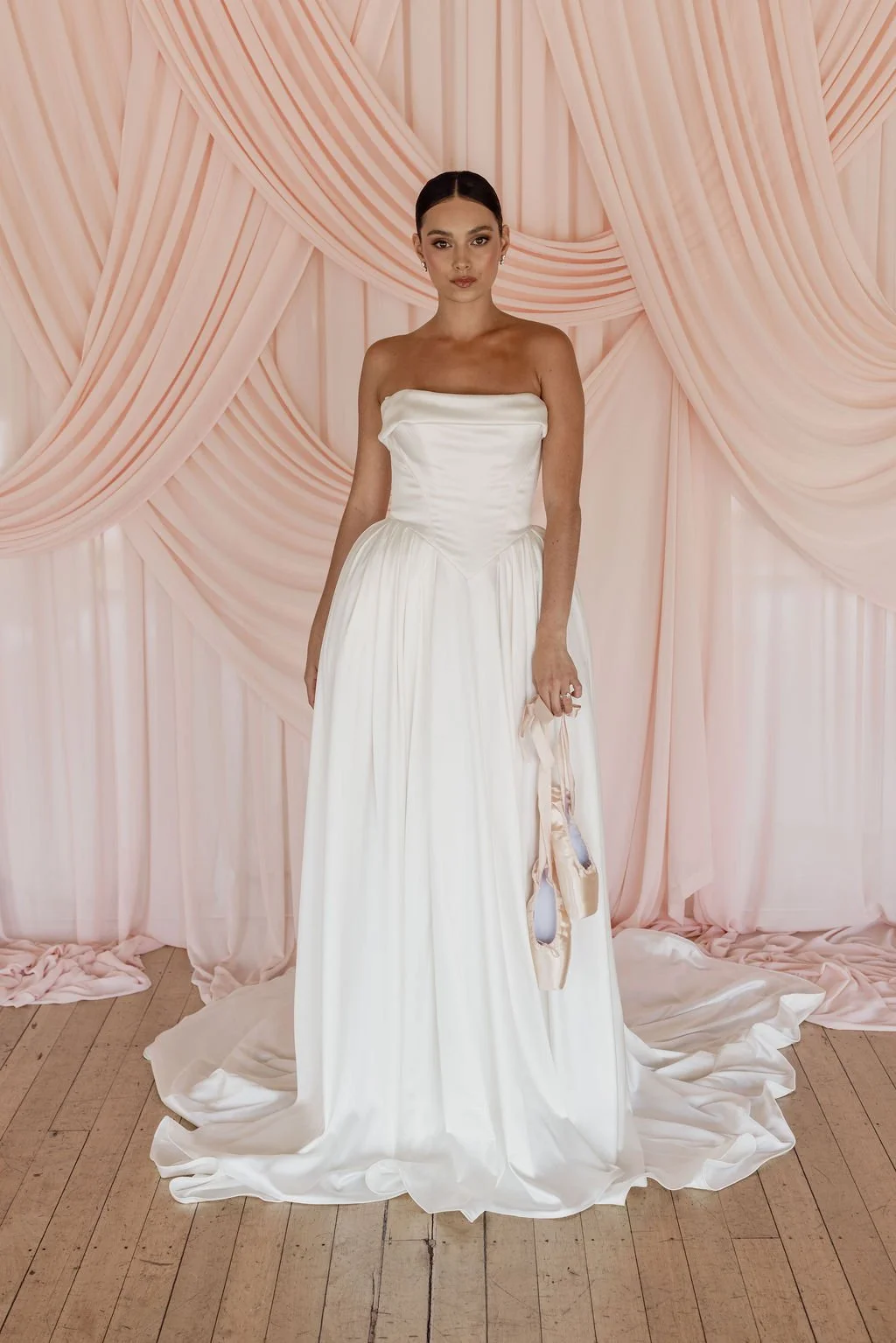 Diana by Trish Peng off-white satin wedding dress with a draped off-the-shoulder neckline, structured basque waist, A-line skirt and detachable bustle, available at Spellbound Bridal Ireland.