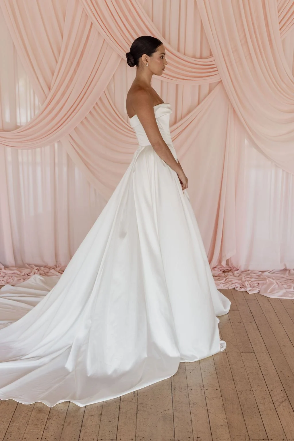Diana by Trish Peng off-white satin wedding dress with a draped off-the-shoulder neckline, structured basque waist, A-line skirt and detachable bustle, available at Spellbound Bridal Ireland.