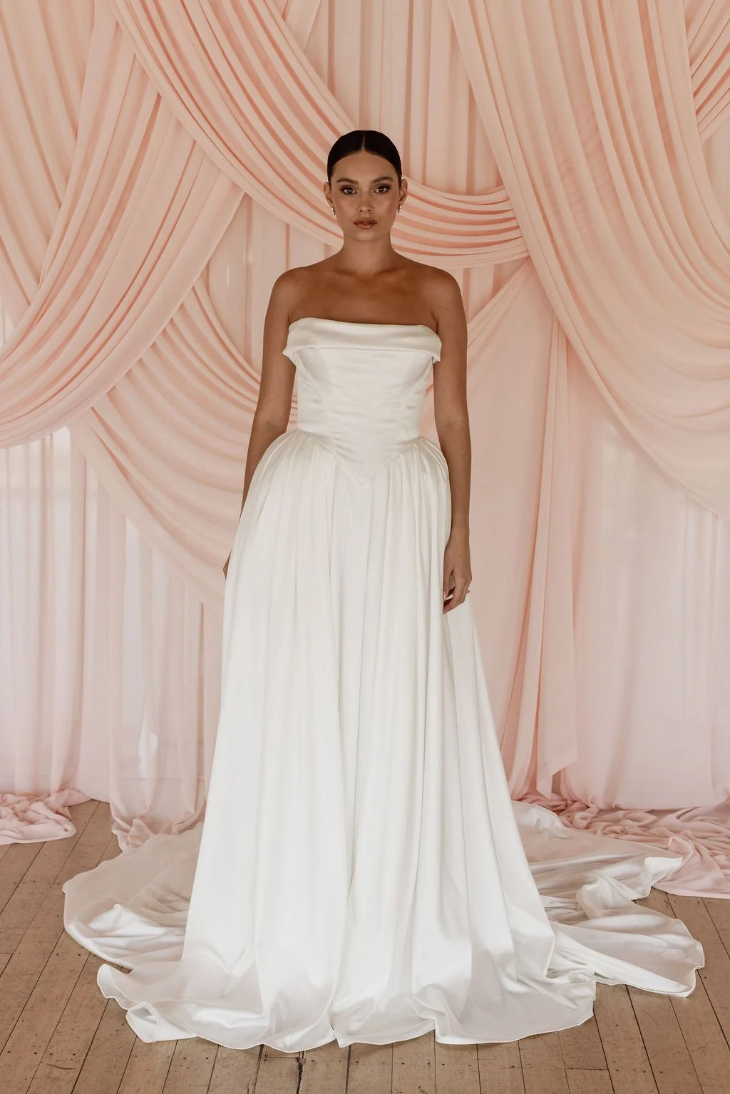 Diana by Trish Peng off-white satin wedding dress with a draped off-the-shoulder neckline, structured basque waist, A-line skirt and detachable bustle, available at Spellbound Bridal Ireland.