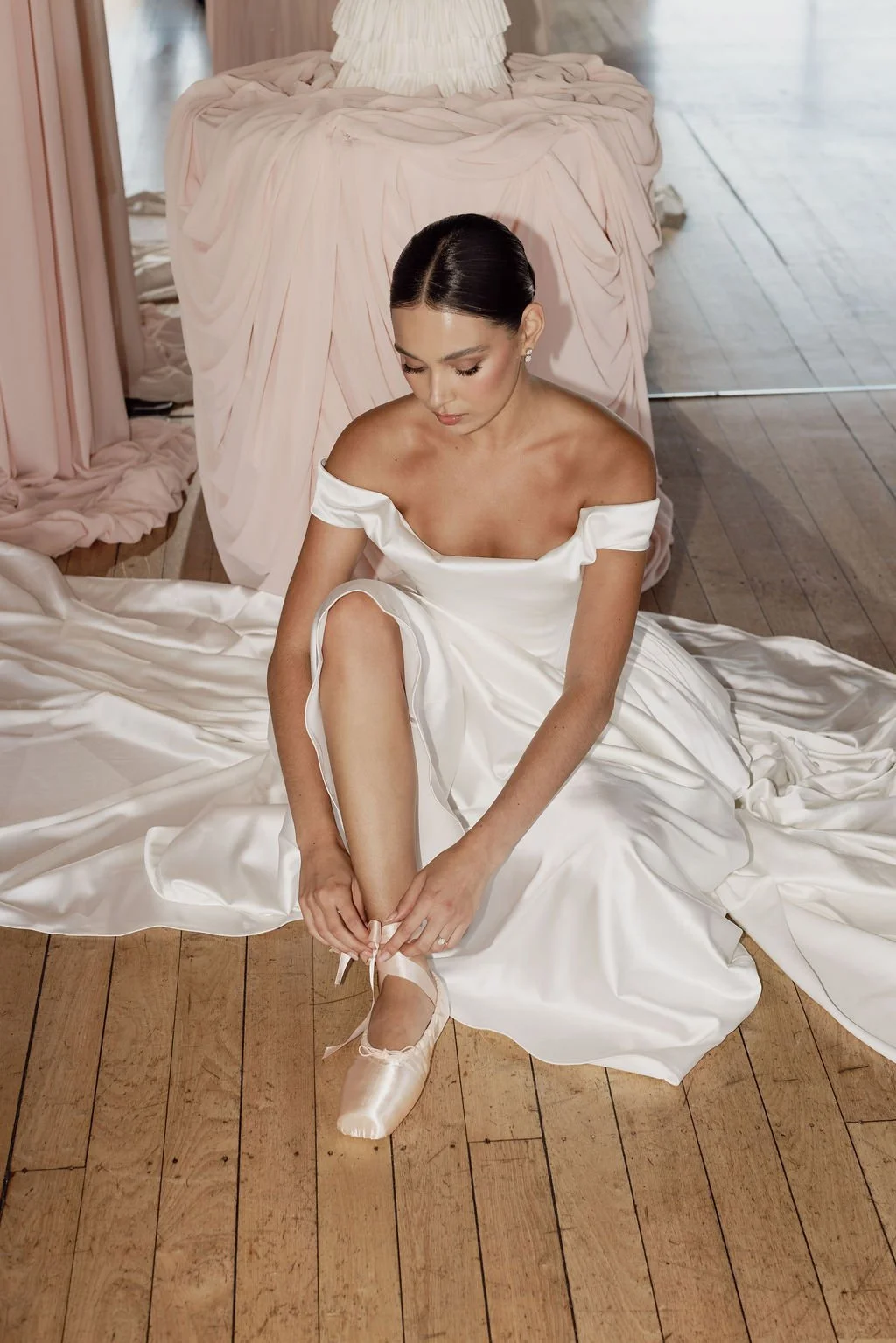 Diana by Trish Peng off-white satin wedding dress with a draped off-the-shoulder neckline, structured basque waist, A-line skirt and detachable bustle, available at Spellbound Bridal Ireland.