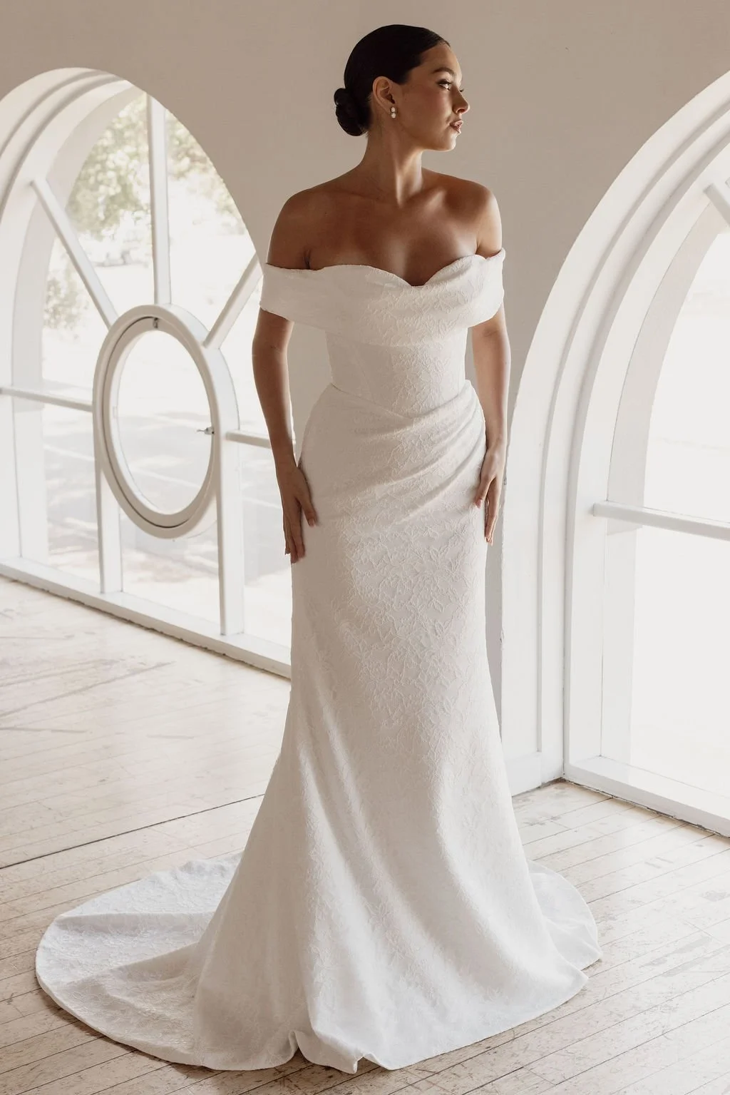 Rosalie by Trish Peng fitted Chantilly lace wedding dress featuring a soft sweetheart off-the-shoulder neckline, draped bodice, ruched skirt and sculpted hourglass silhouette, available at Spellbound Bridal Ireland.
