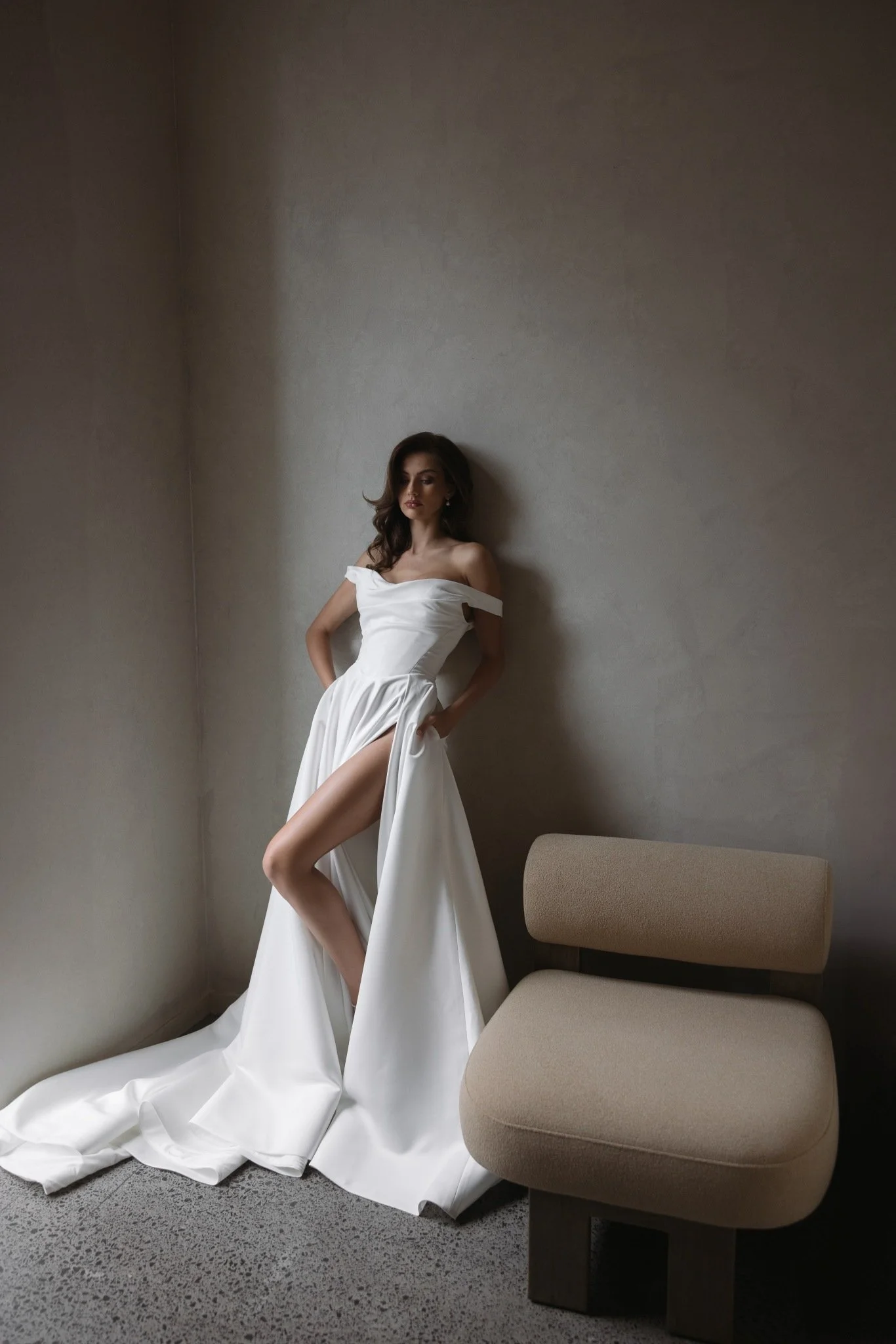 Emily by Trish Peng matte satin wedding dress featuring a draped off-the-shoulder neckline, ruched bodice, sculpted basque waist, A-line skirt and dramatic side split, available at Spellbound Bridal Ireland.
