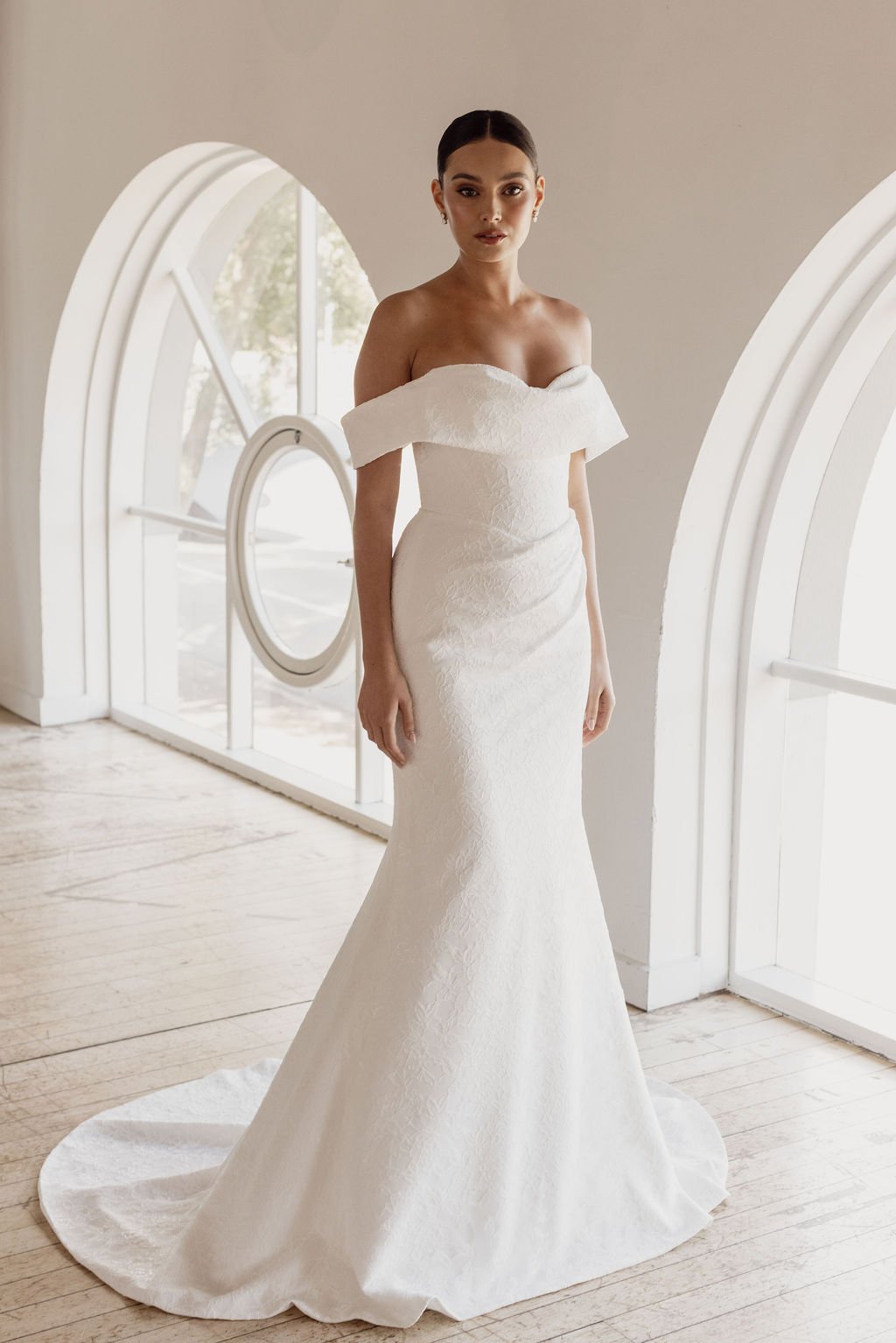 Rosalie by Trish Peng fitted Chantilly lace wedding dress featuring a soft sweetheart off-the-shoulder neckline, draped bodice, ruched skirt and sculpted hourglass silhouette, available at Spellbound Bridal Ireland.
