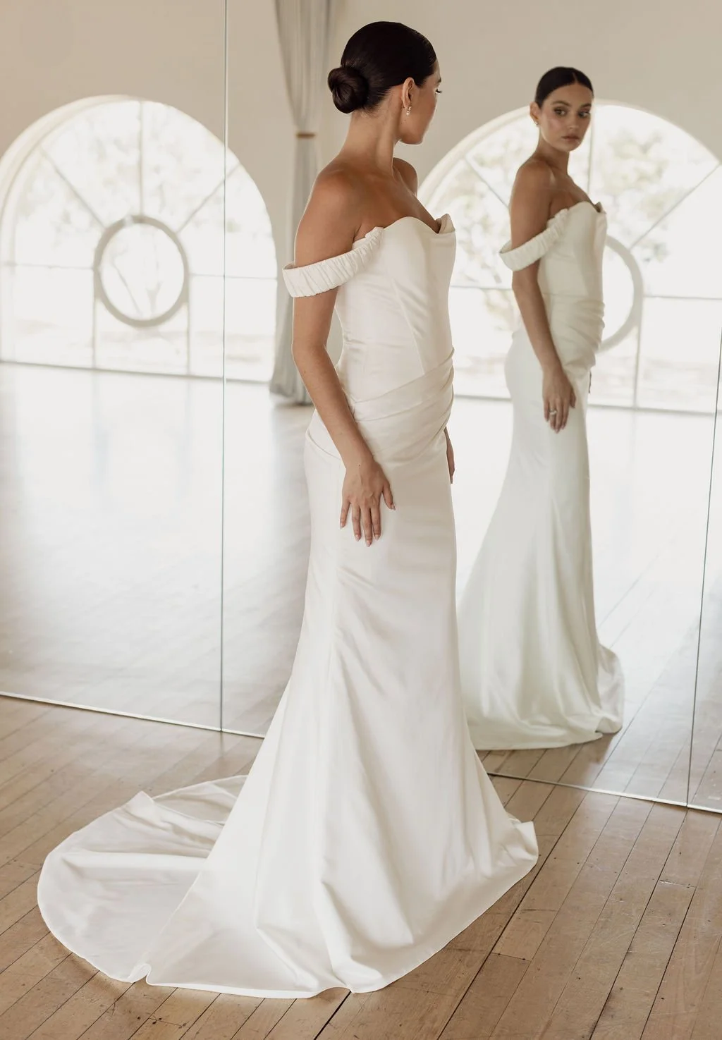Demi by Trish Peng fitted satin crepe wedding dress featuring an asymmetric draped bodice, off-the-shoulder cowl neckline, removable straps and softly ruched skirt, available at Spellbound Bridal Ireland.
