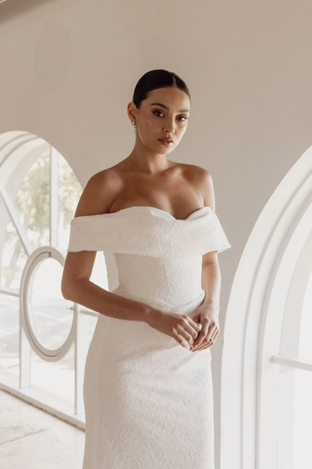 Rosalie by Trish Peng fitted Chantilly lace wedding dress featuring a soft sweetheart off-the-shoulder neckline, draped bodice, ruched skirt and sculpted hourglass silhouette, available at Spellbound Bridal Ireland.
