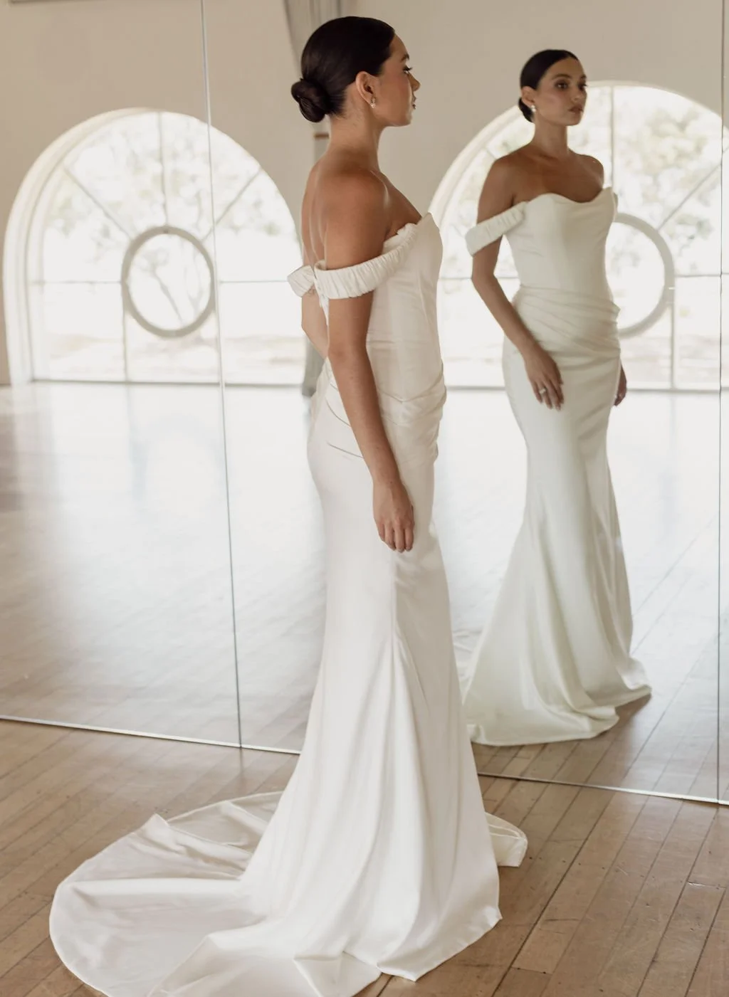 Demi by Trish Peng fitted satin crepe wedding dress featuring an asymmetric draped bodice, off-the-shoulder cowl neckline, removable straps and softly ruched skirt, available at Spellbound Bridal Ireland.
