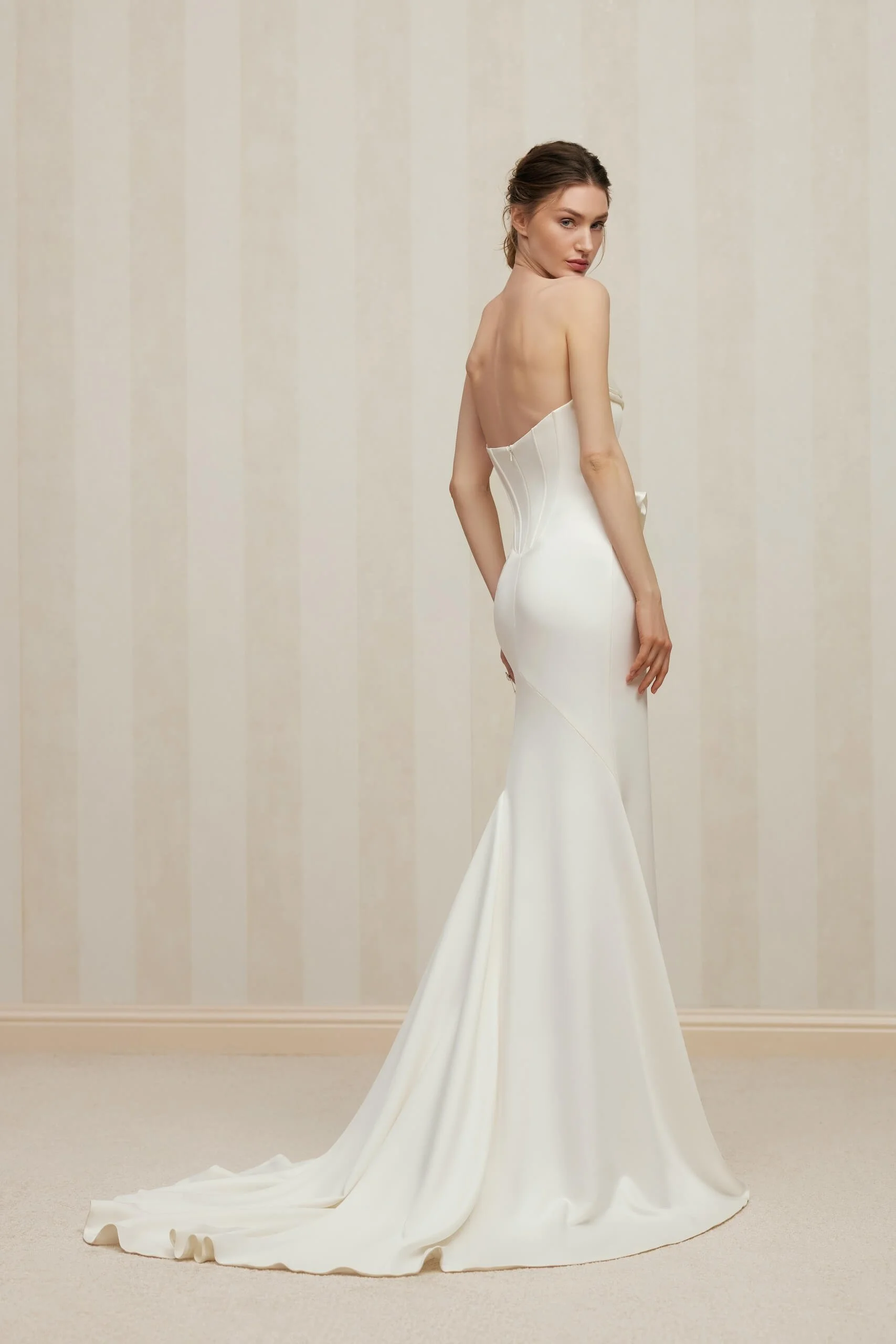 Back view of the FENNA wedding dress by designer Anne-Mariée, featuring a low back, sculpted corset, fitted fit and flare silhouette and flowing chapel train in luxurious ivory satin. Contemporary minimalist bridal gown available exclusively at Spell