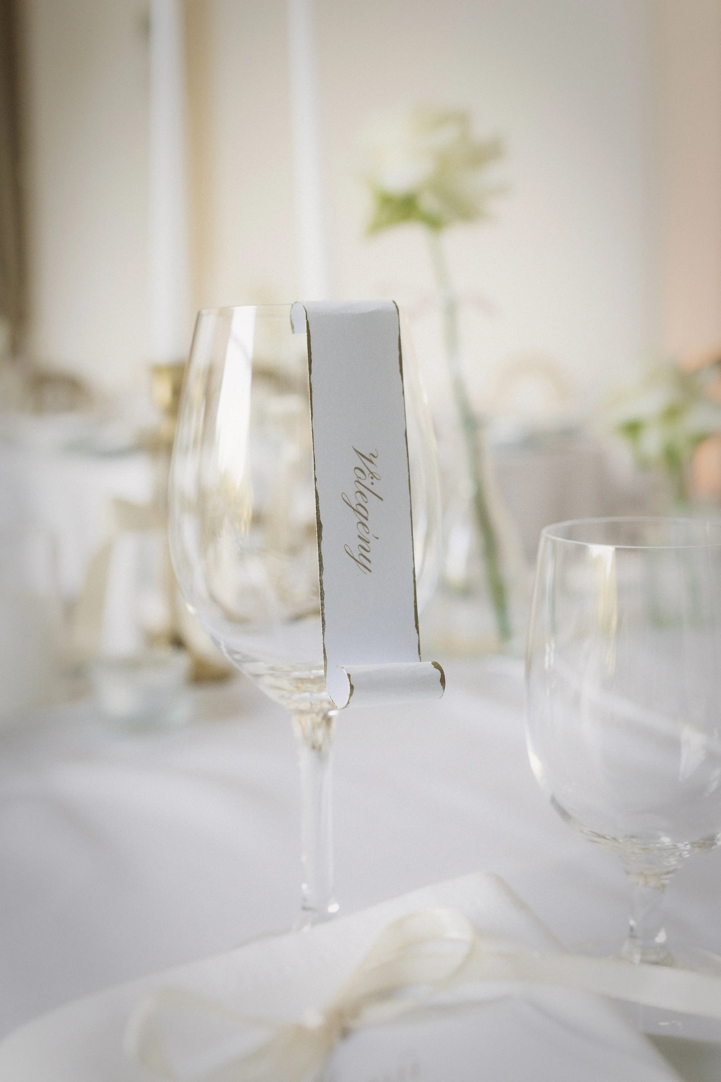 modern esküvői névkártya pohárra helyezve - elegáns vendégültetés megoldás, minimalista esküvői grafika és finom arany tipográfia az esküvői asztaldekor részeként