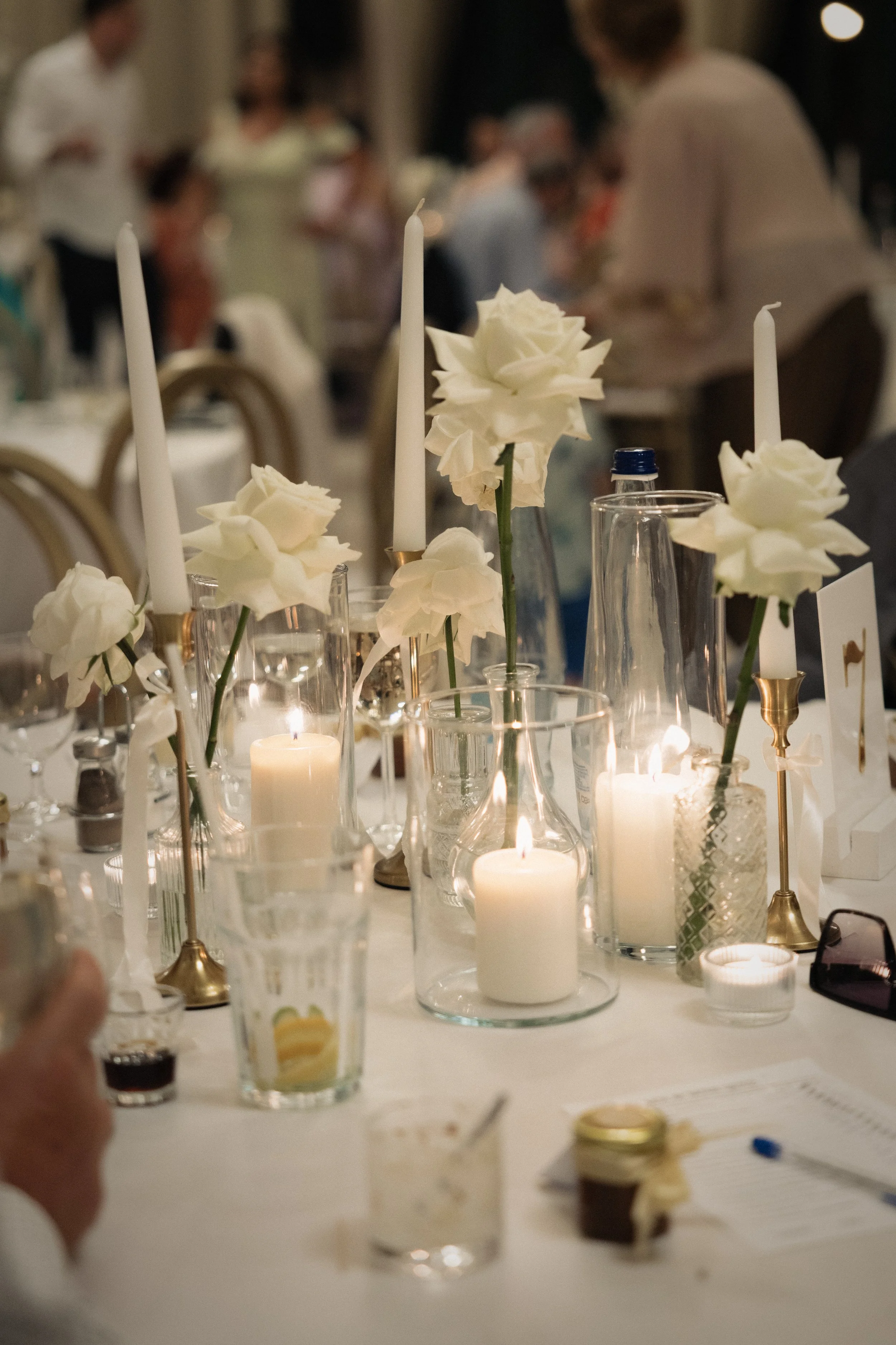 Gyertyafényes esküvői asztaldekor fehér rózsákkal és elegáns üveg kompozícióval - modern esküvői dekoráció vendégasztalon