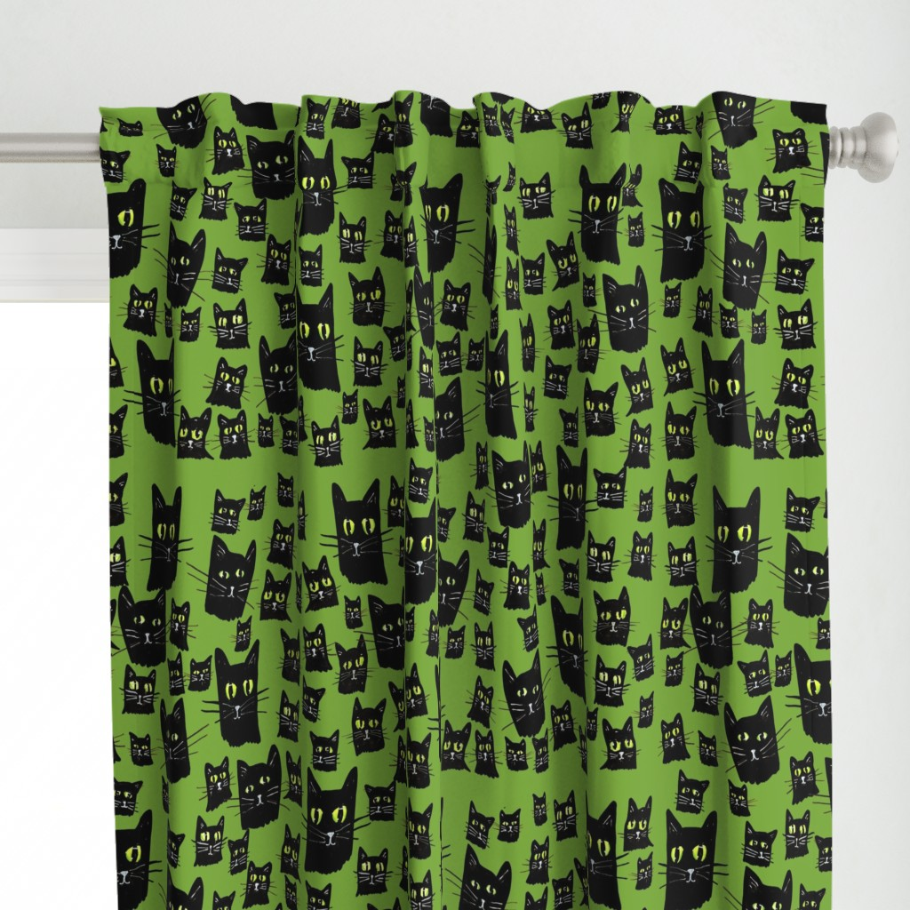 Green curtain with a pattern of black cats with yellow eyes hanging from a silver curtain rod.