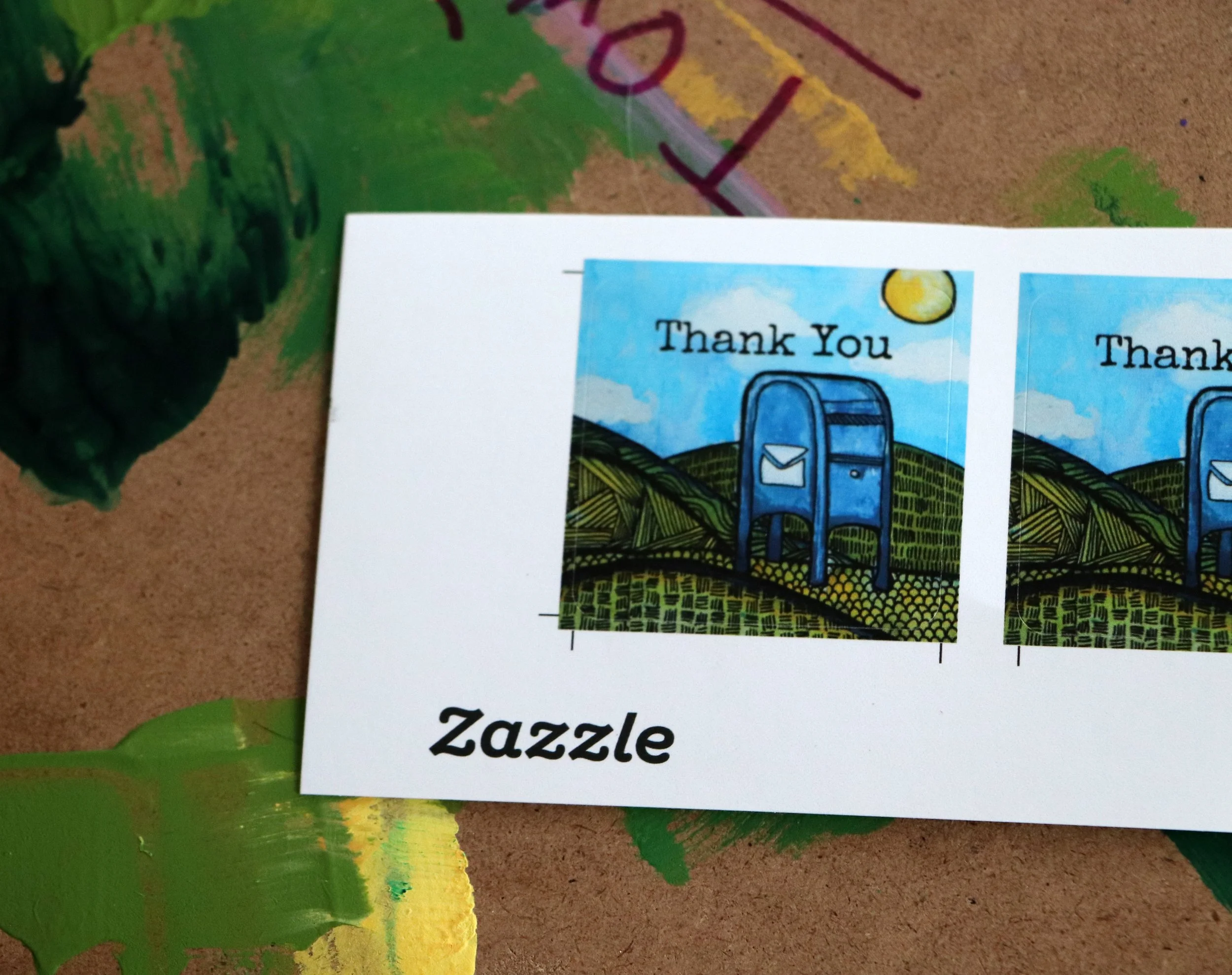 A sheet of paper with Zazzle logo and two colorful postage stamp designs featuring a mail carrier mailbox on a rural landscape with the words "Thank You" at the top of each stamp.