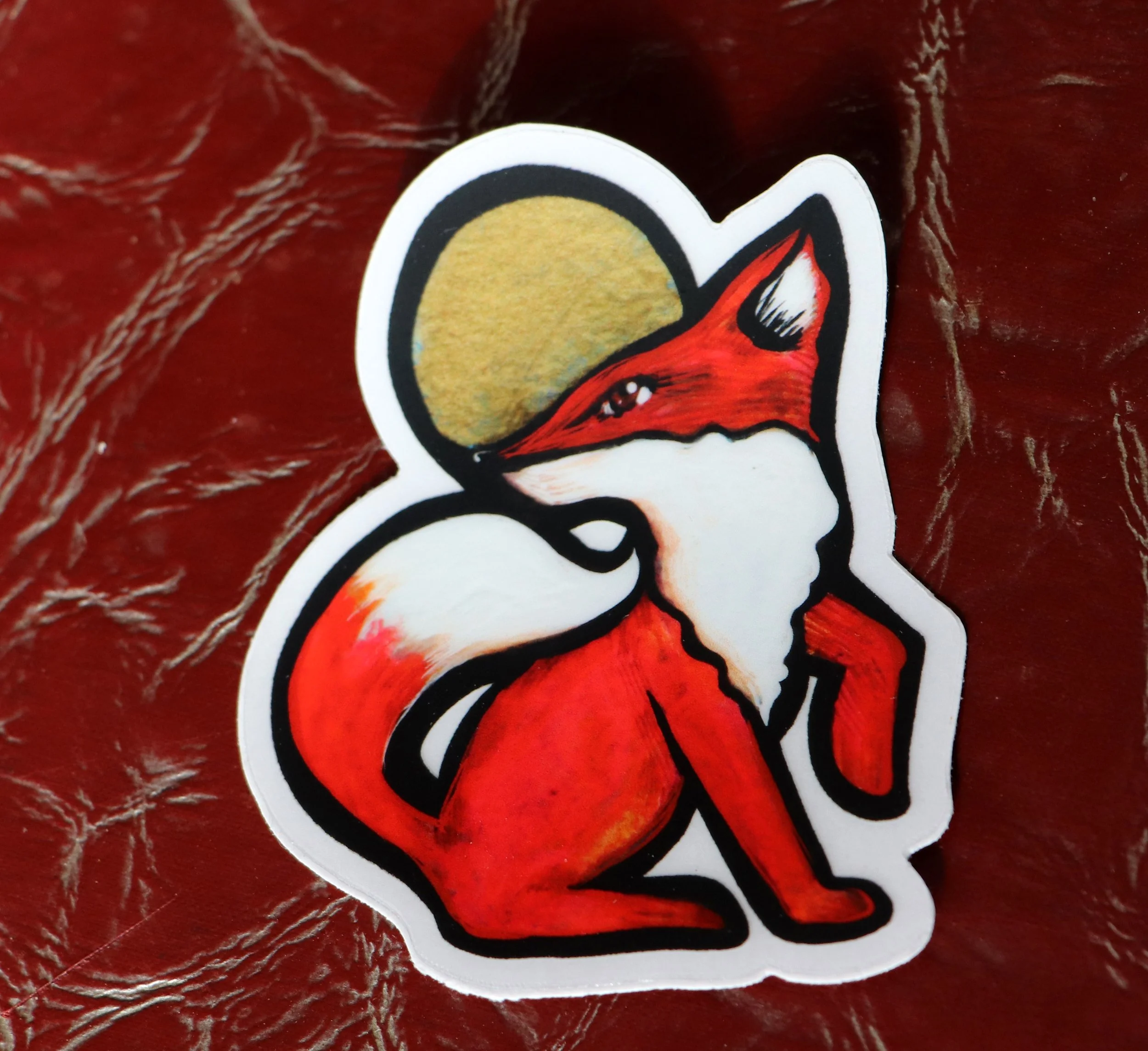 A colorful sticker of a red fox with black and white accents, set against a red textured background.