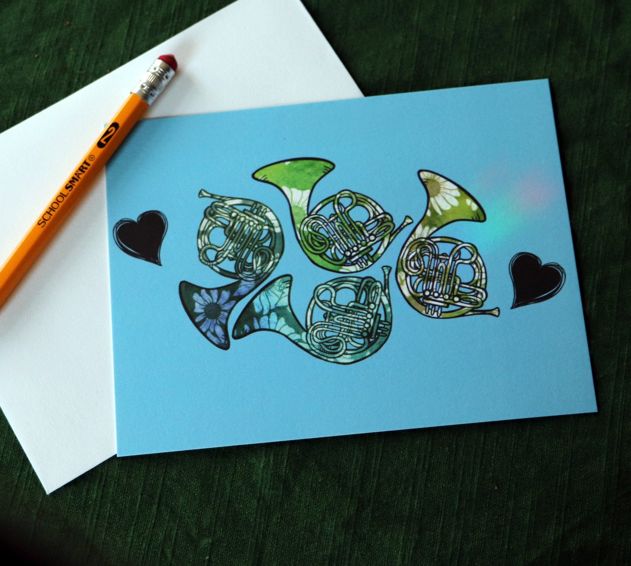 Colorful artwork of five French horns on a blue background, with two black heart shapes and a white envelope and orange pencil nearby.