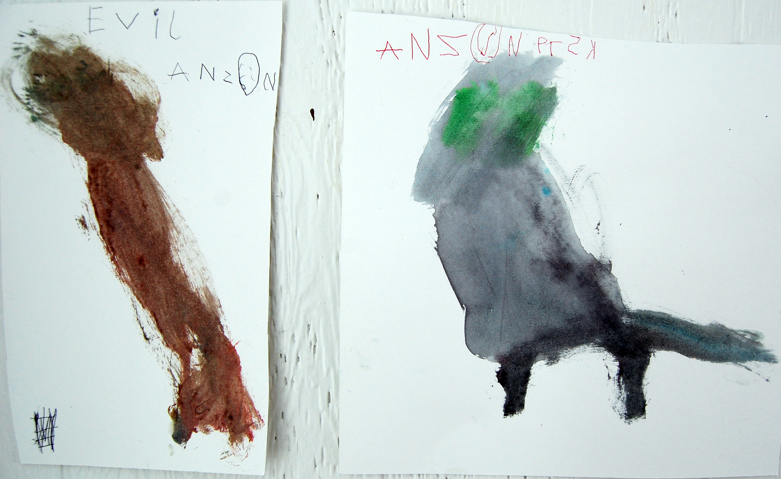Two abstract watercolor paintings on paper. The left painting features a brown-colored figure with a handwritten label 'Evil' above it. The right painting depicts a dark-colored figure with green and gray patches at the top and a handwritten label in