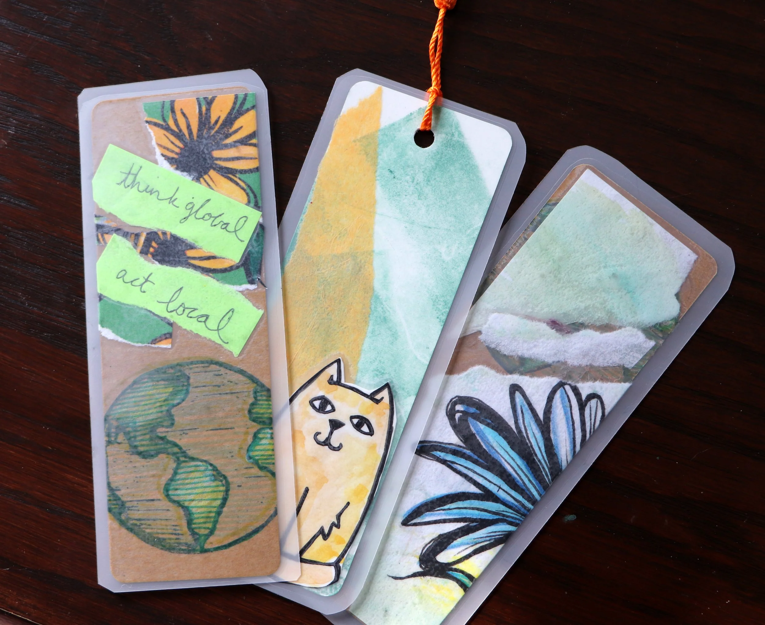 Three handmade bookmarks with watercolor illustrations and handwritten notes on a wooden surface.