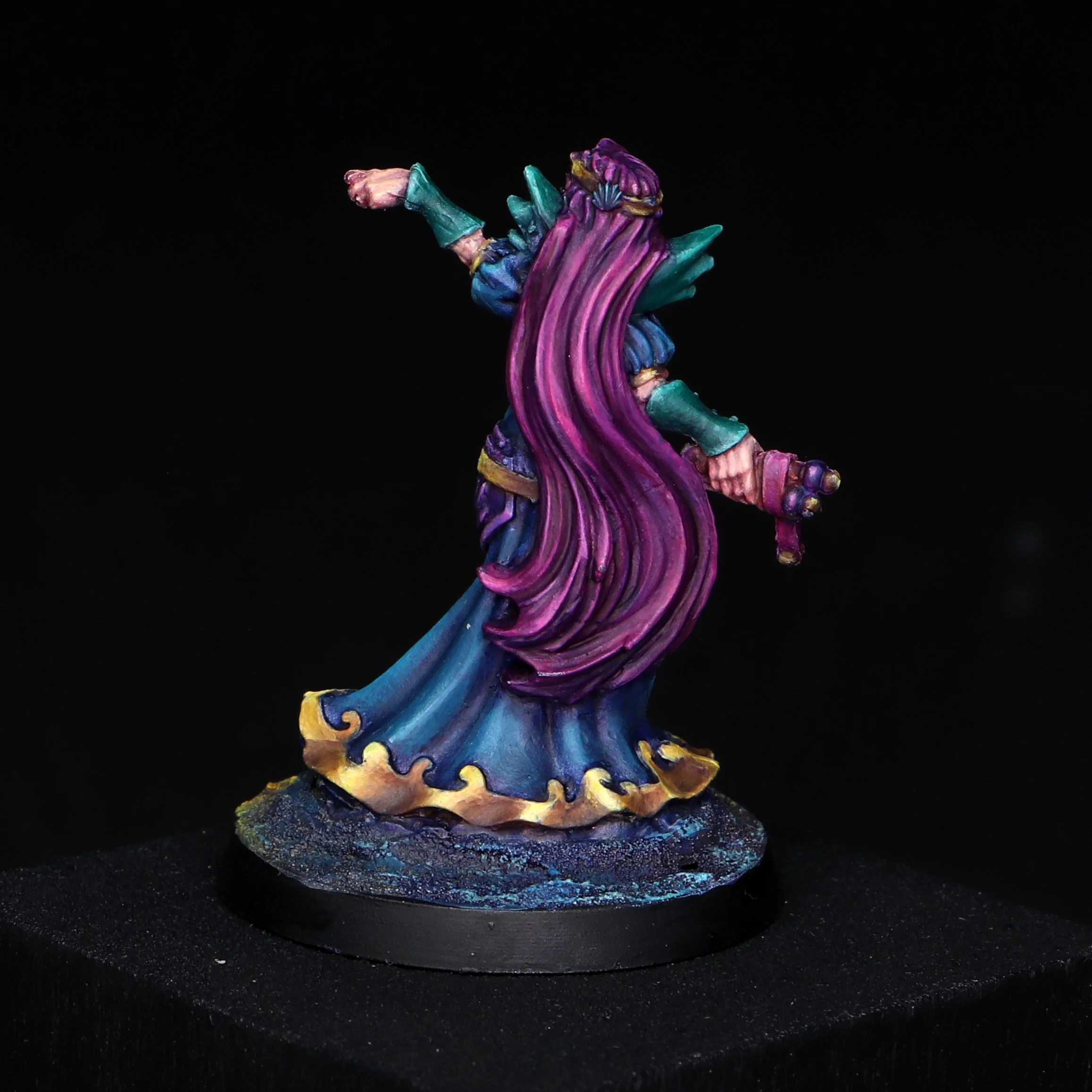 Colorful fantasy figurine with purple, blue, green, and yellow accents, standing on a textured black base against a black background.