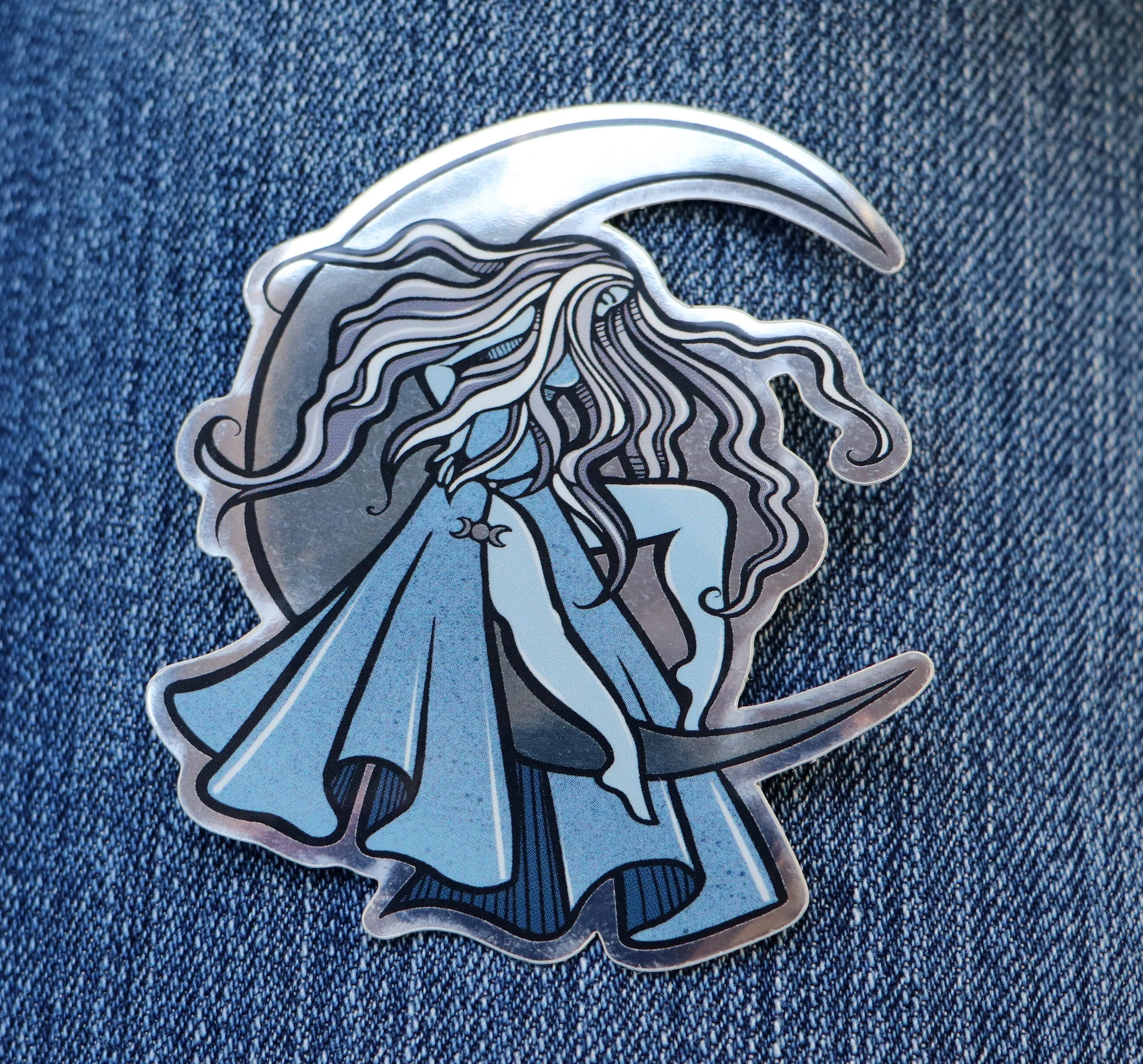 A metallic sticker of a woman with long, flowing hair and a headpiece, placed on a dark blue denim fabric background.