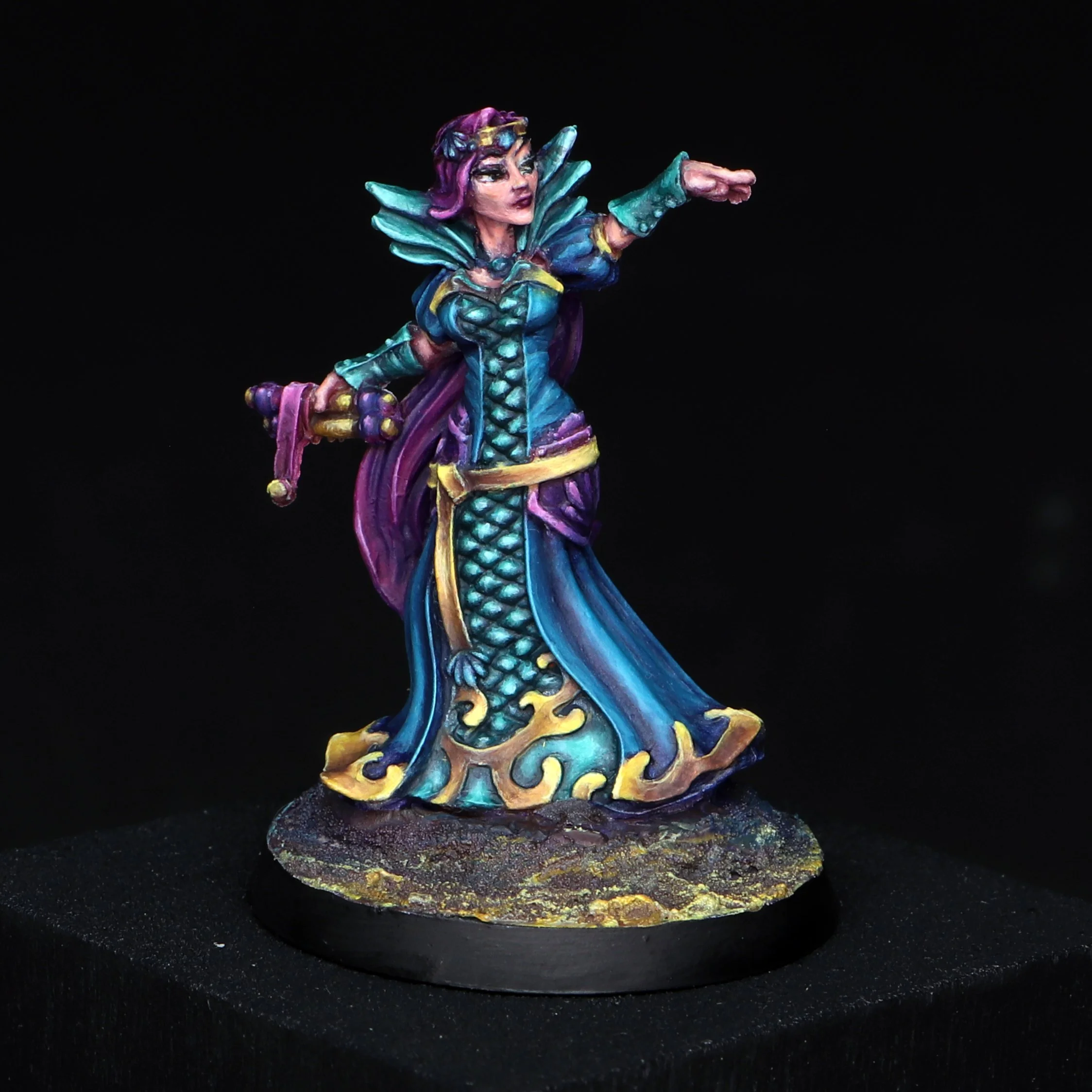Colorful miniature figurine of a fantasy character with purple hair, green wings, and blue and yellow clothing, standing on a painted circular base.