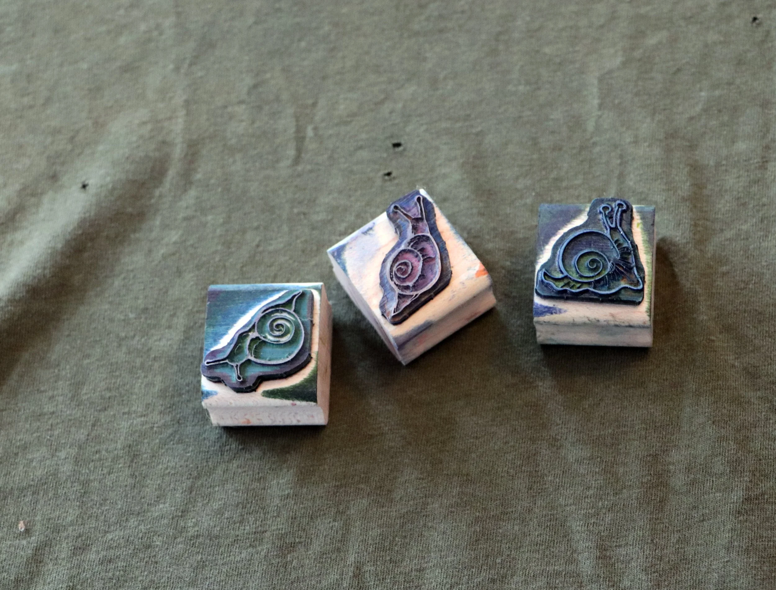Three rubber stamps with snail designs on a green fabric surface.
