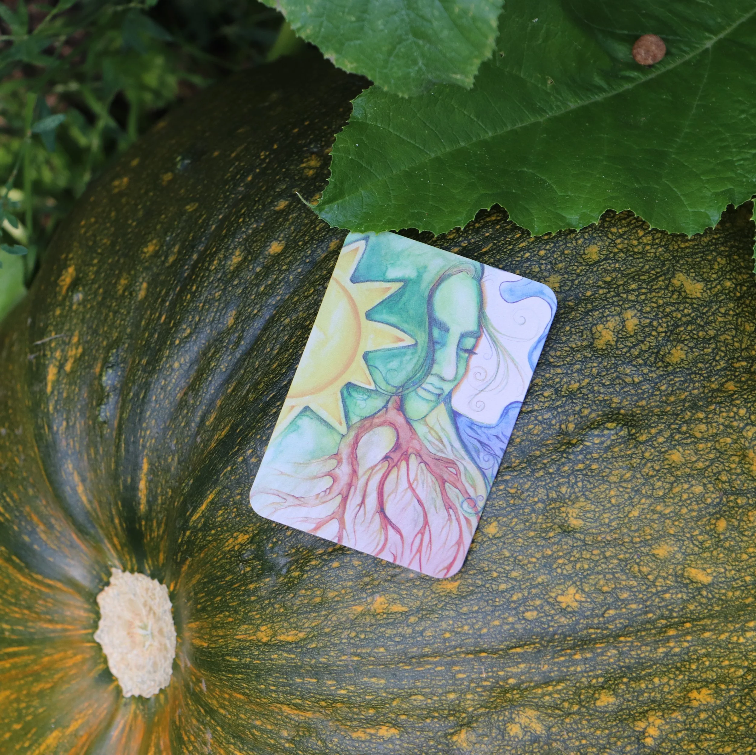 A colorful illustration of a woman with green hair, a sun near her head, and roots extending from her chest, placed on a large green and yellow pumpkin outside among green leaves.