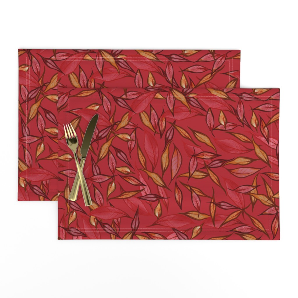 Two red leaf-patterned placemats with gold-colored cutlery (fork and knife) on top.