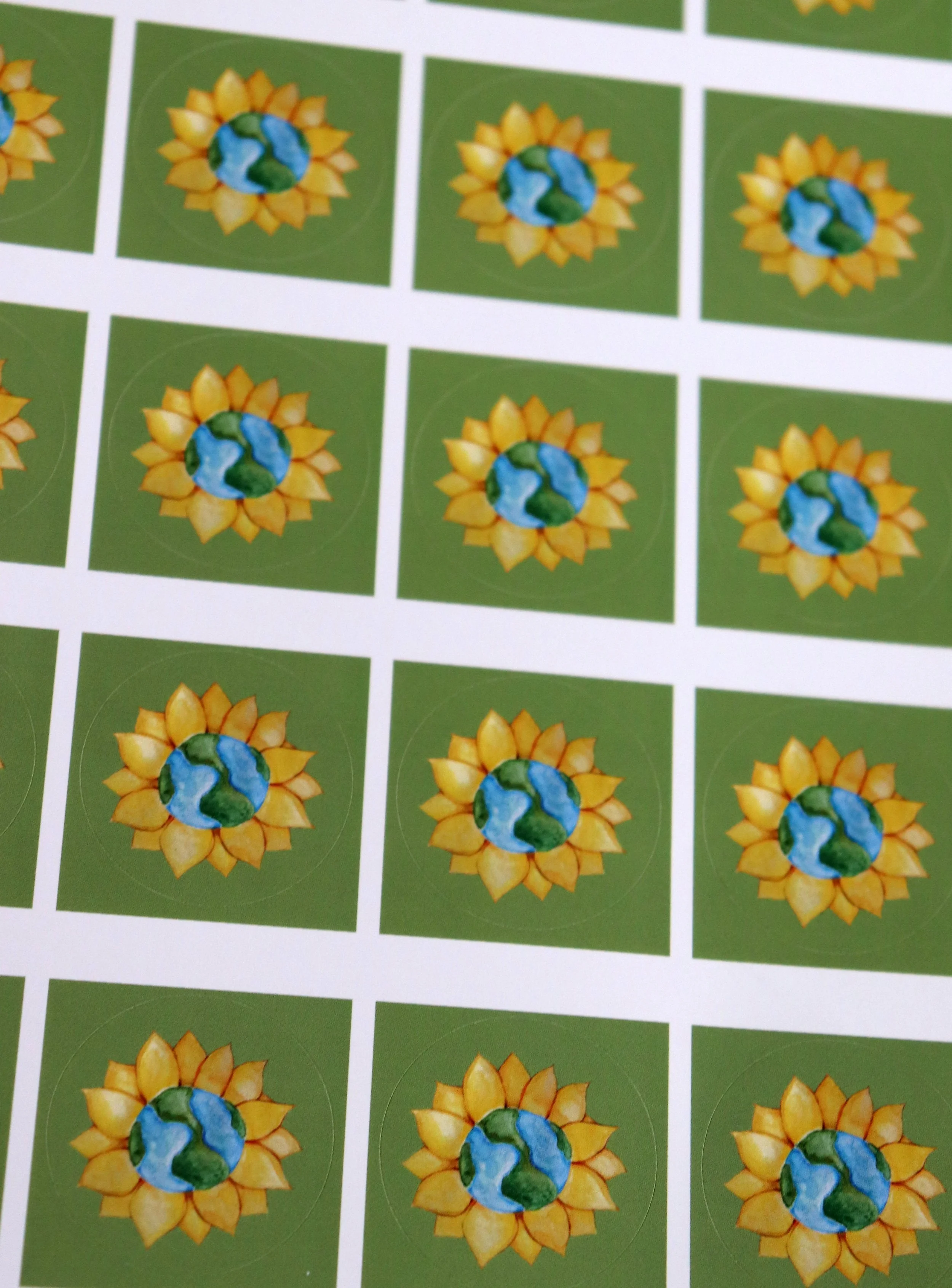 Sheet of stickers featuring a sunflower with a globe in the center, representing Earth, on a green background.