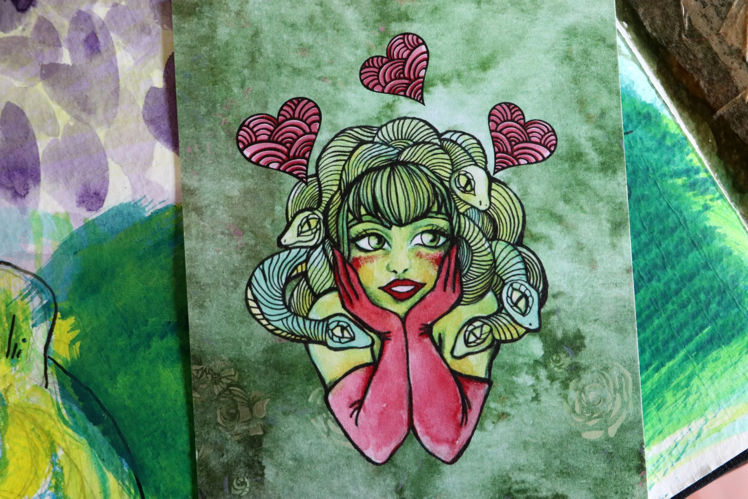 Colorful illustration of a woman with green skin, large green eyes, and long flowing hair. She is holding her chin with her hands and has various pink hearts and pink petal-like shapes above her head.