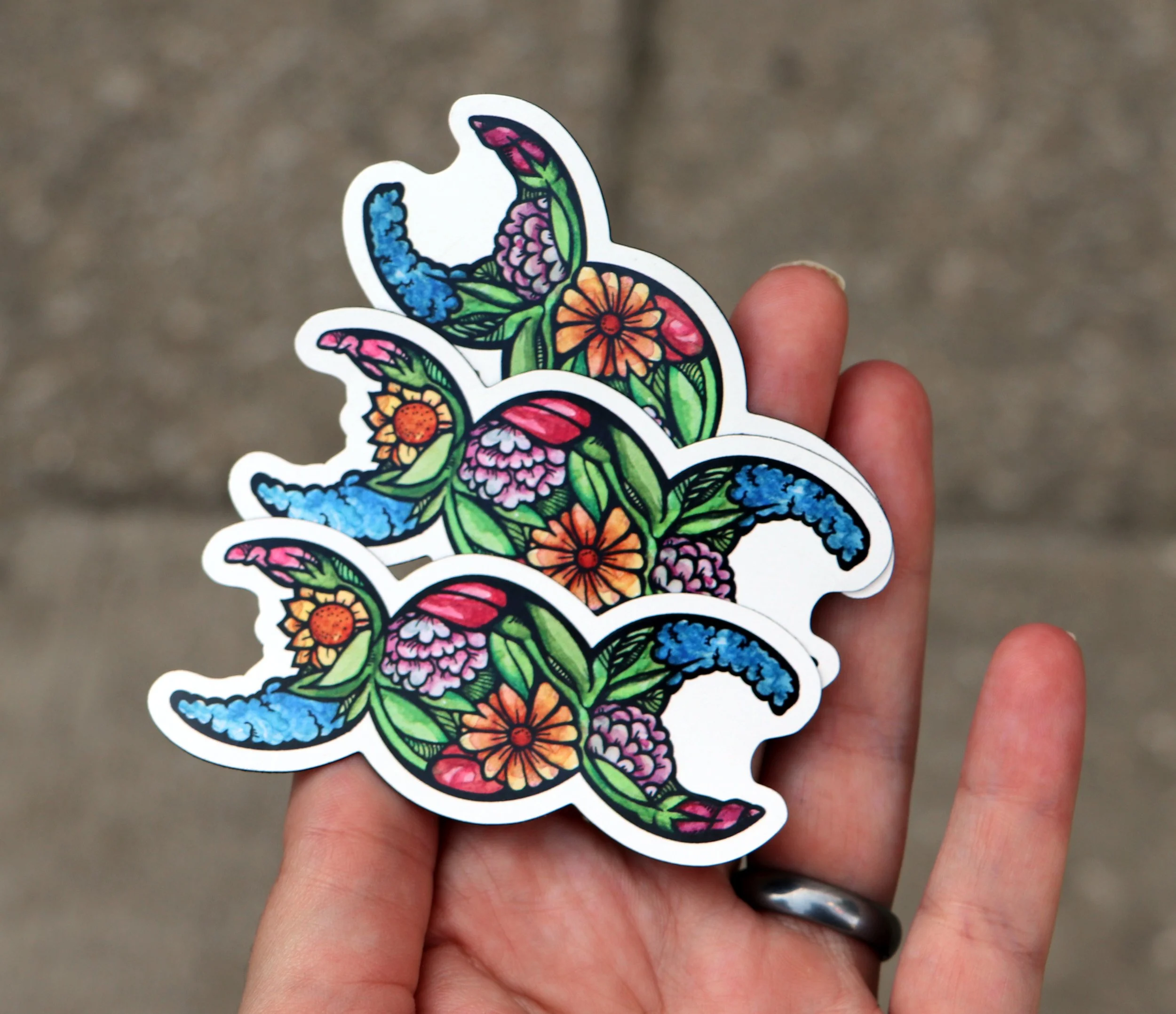 Colorful sticker of a snake made of floral patterns being held between two fingers.