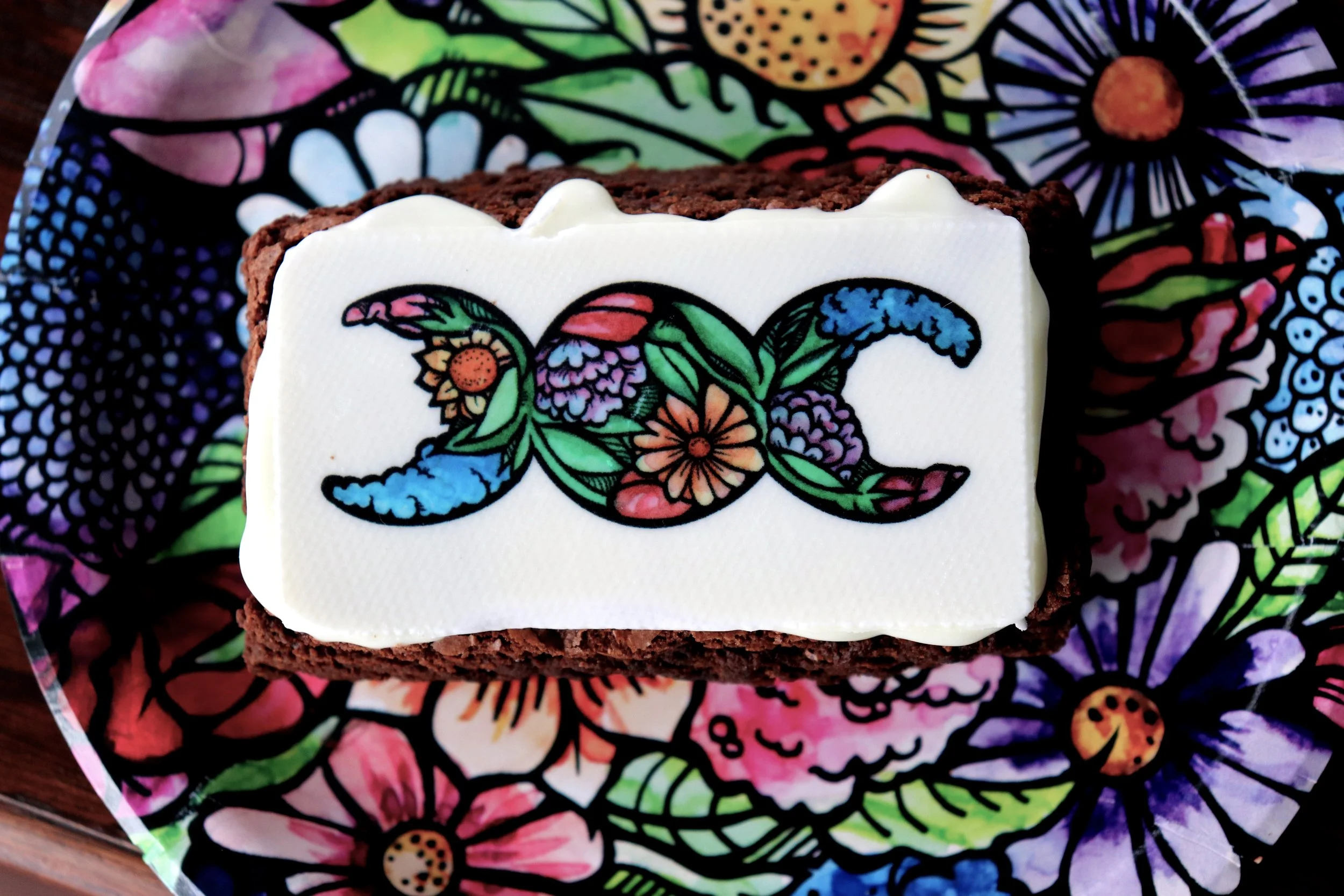 A rectangular piece of cake with white icing and colorful floral and leaf designs on top, placed on a floral patterned napkin.