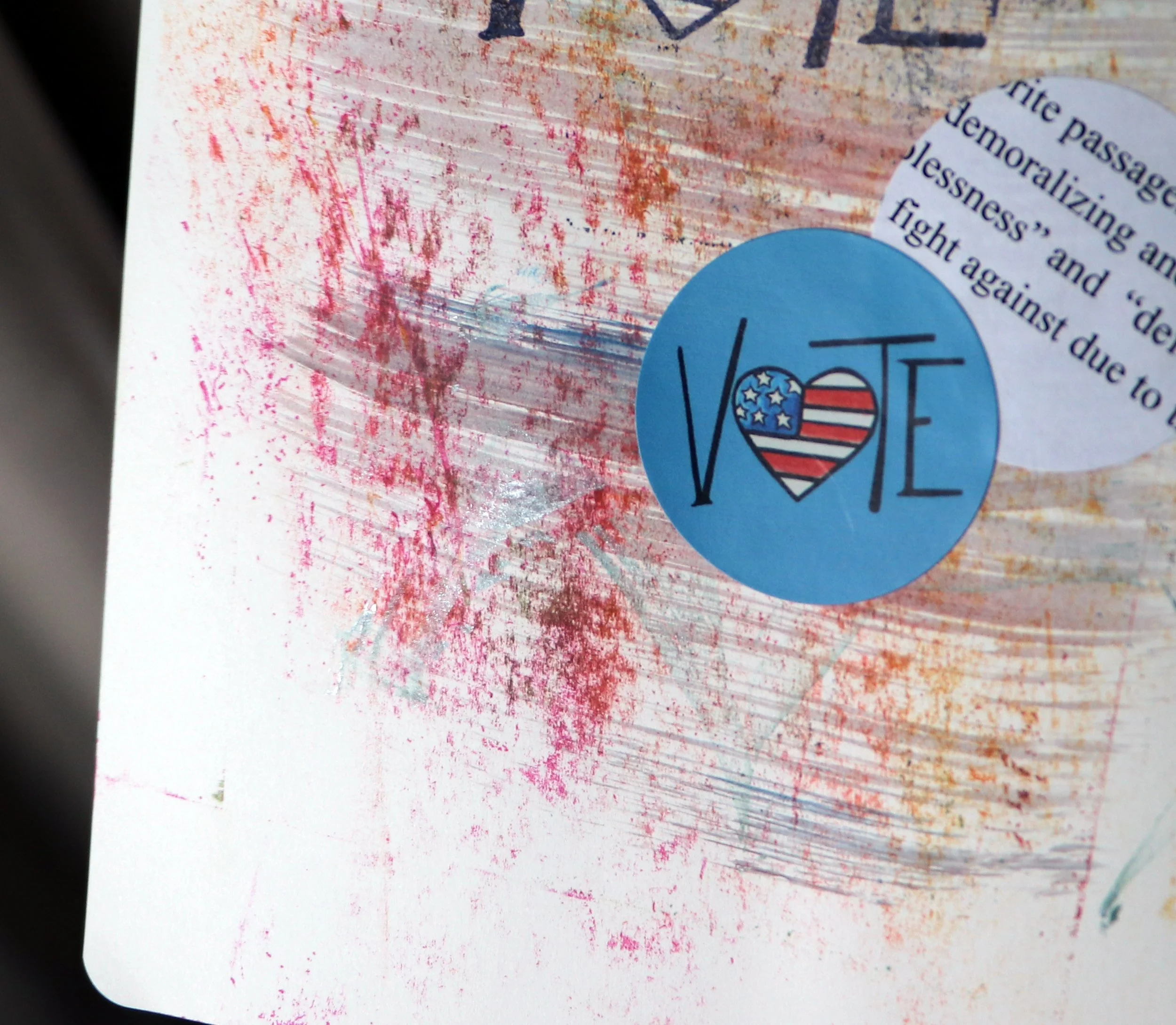 A paper with red and pink paint streaks and a blue vote sticker that features a heart with the American flag design, along with some partial text.