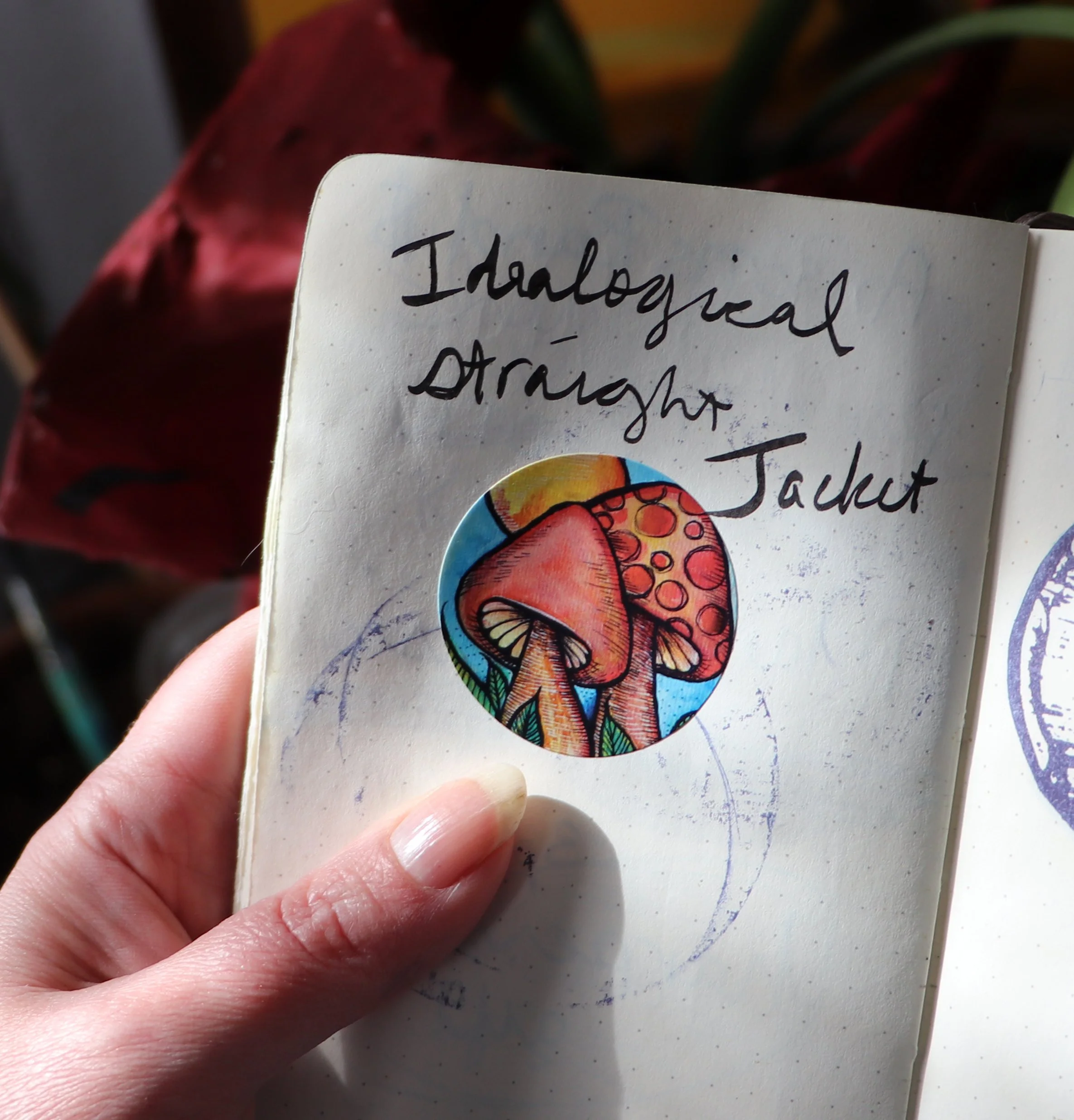 A handwritten note on a page that reads 'Ideological Strough Jacket' with a colorful sticker of mushrooms underneath the text.