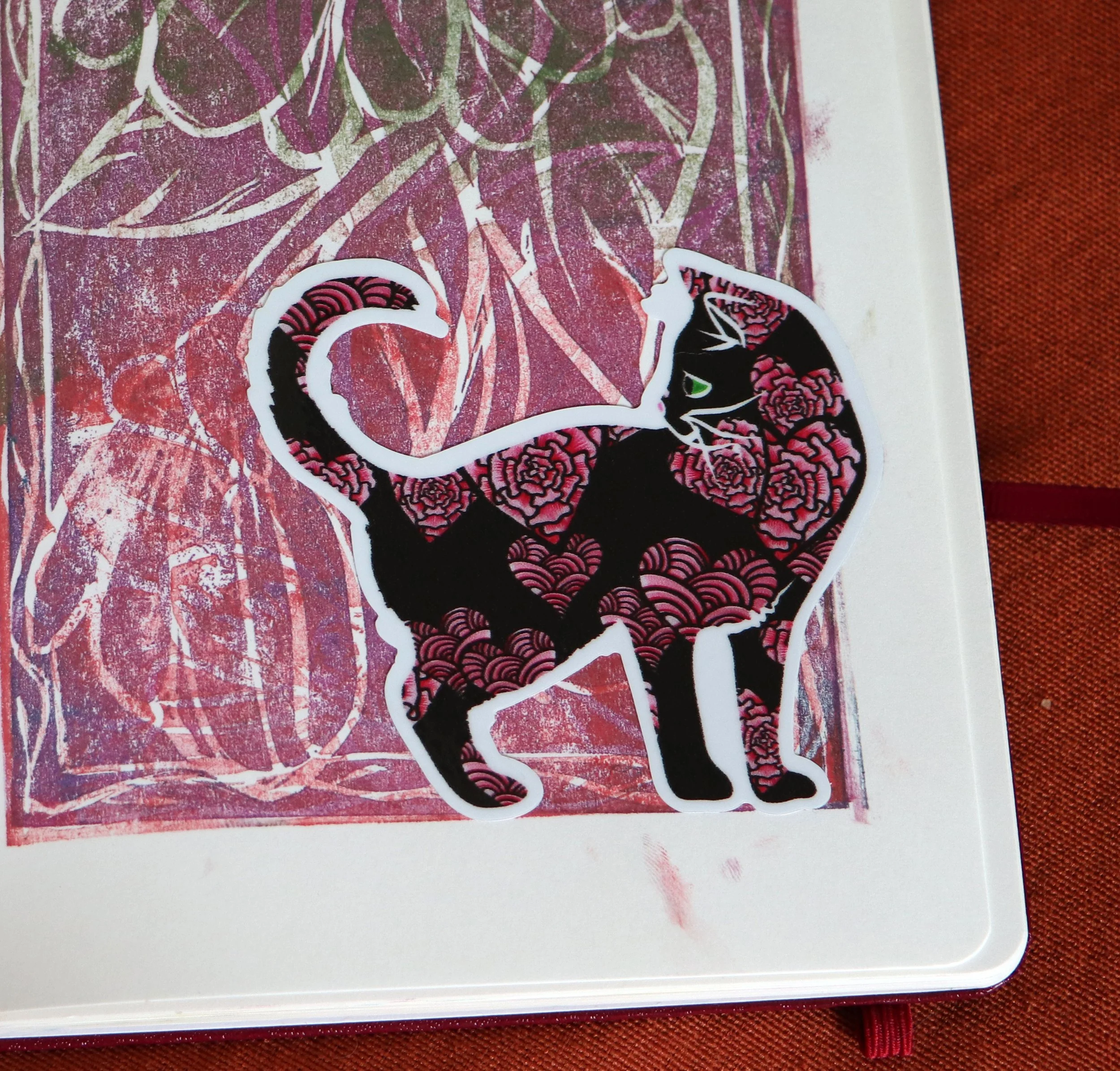 Sticker of a black cat with pink lotus patterns on a red and pink background.