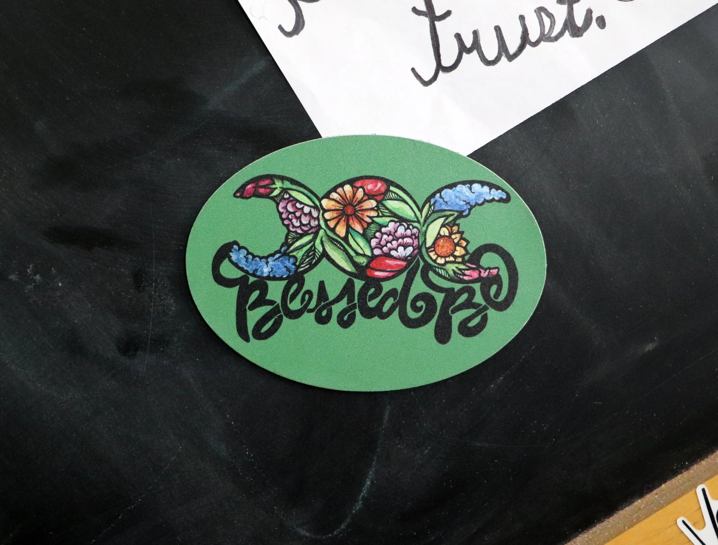 A green oval sticker with colorful flowers and the word "Blessed" written in black cursive script.