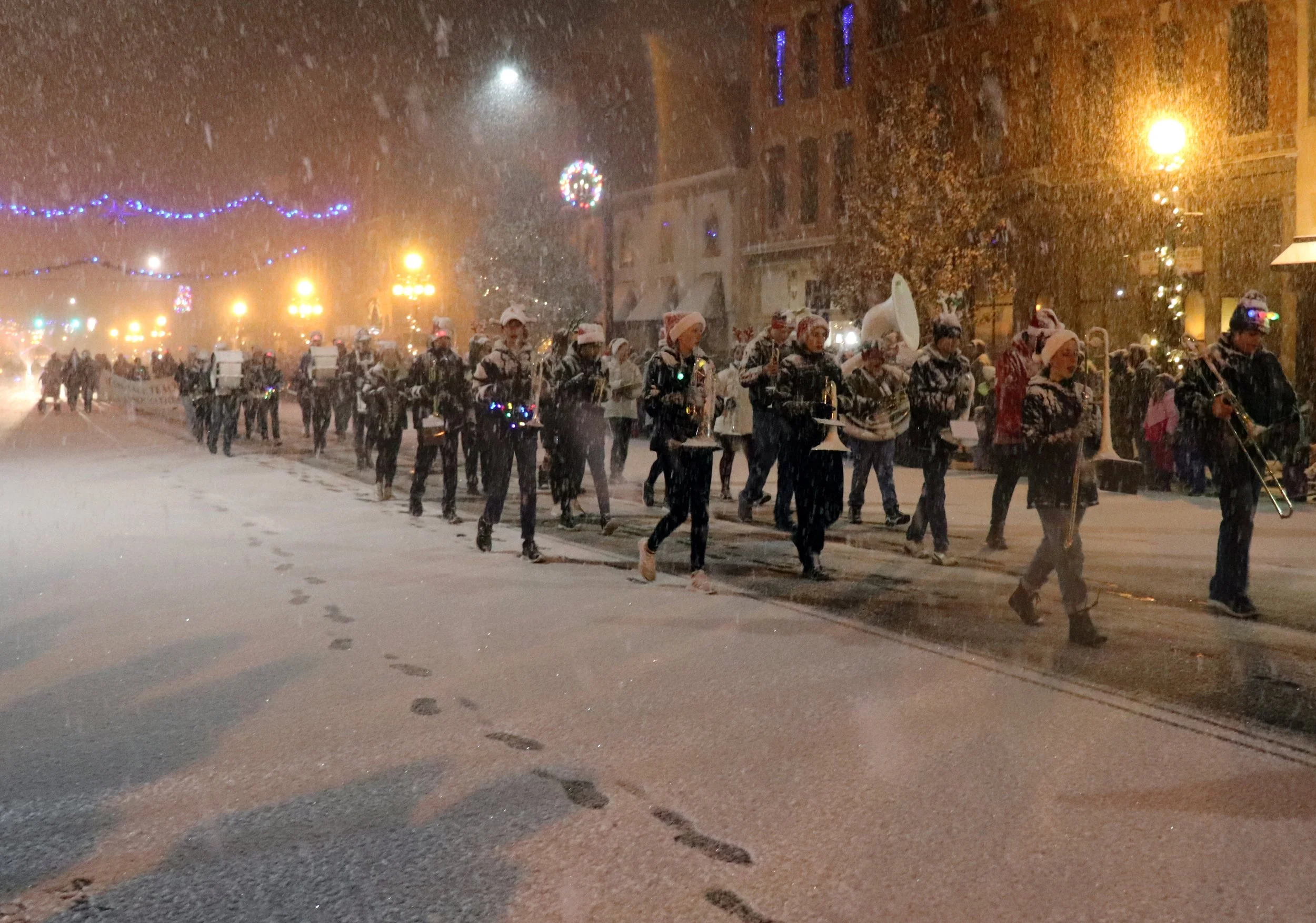 A magical Marshall, Michigan Christmas Parade scene: the Marshall High School Redhawks Marching Band performs in the snowy streets. Dressed in vibrant reds, their music echoes through the winter wonderland, embodying holiday cheer. Perfect for earth 