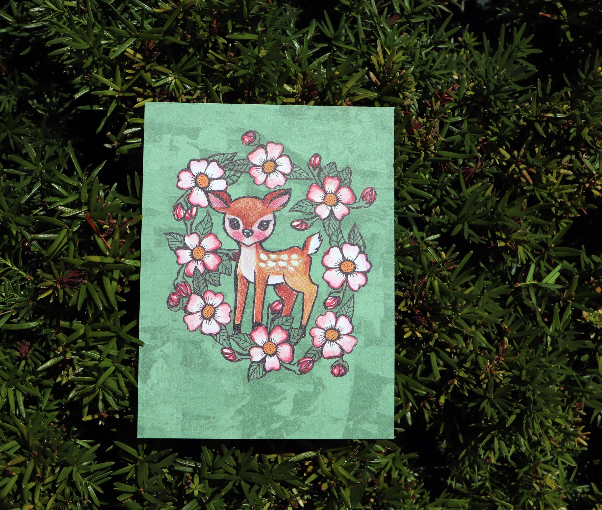 Colorful illustration of a deer with pink flowers and green leaves on a green background.