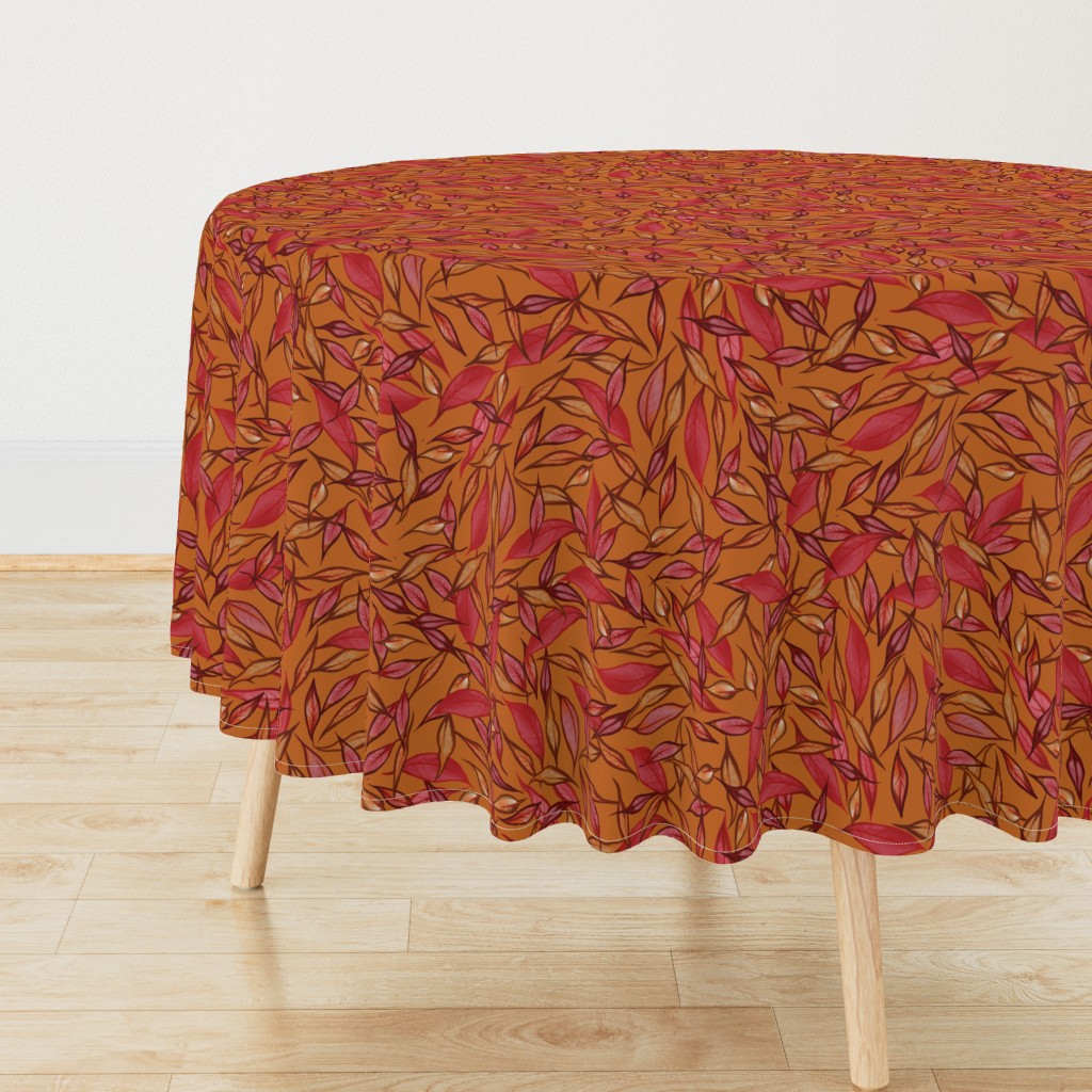 Round table with a leaf-patterned tablecloth in shades of red and orange, with light wood legs, placed on a wooden floor against a plain white wall.
