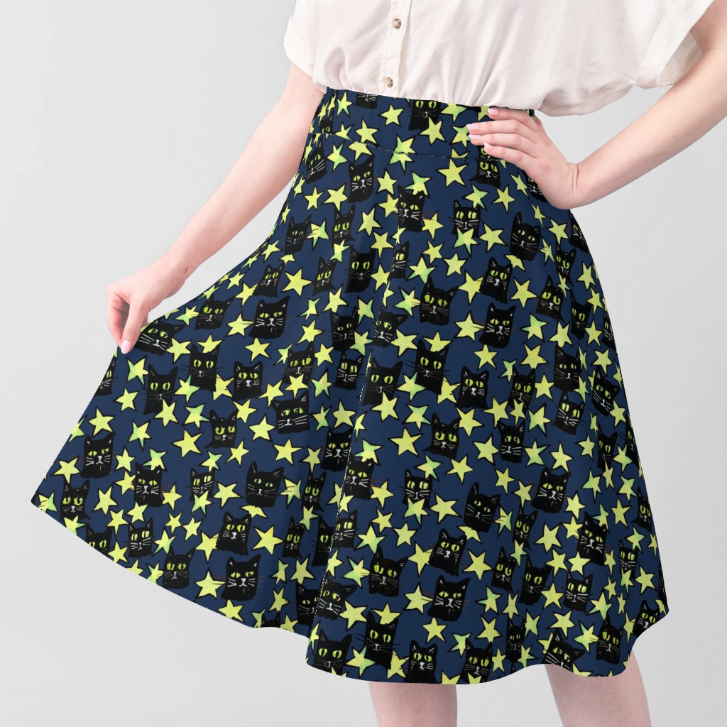 A woman wearing a navy blue skirt with a pattern of black cats and yellow stars, paired with a beige blouse.