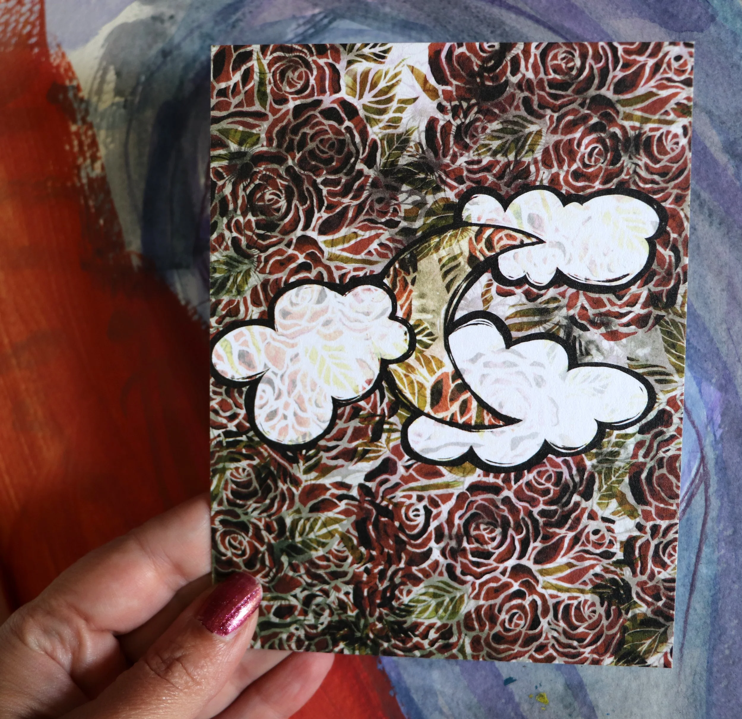 Close-up of a hand holding a card with a floral and leaf pattern, featuring white, brown, green, and black accents, with a colorful background.