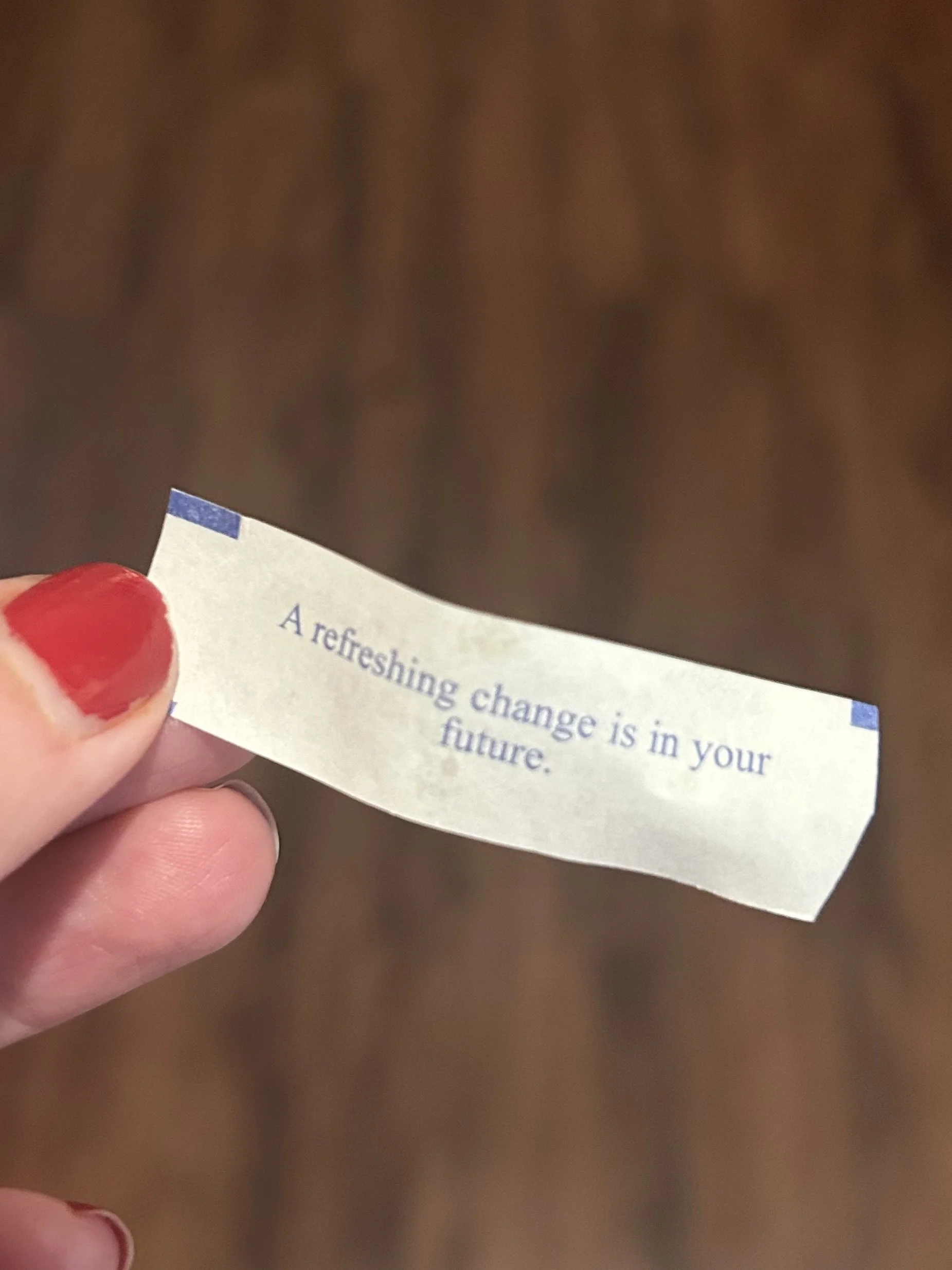 fingers with chipped red nail polish hold a fortune cookie with the text "a refreshing change is in your future"