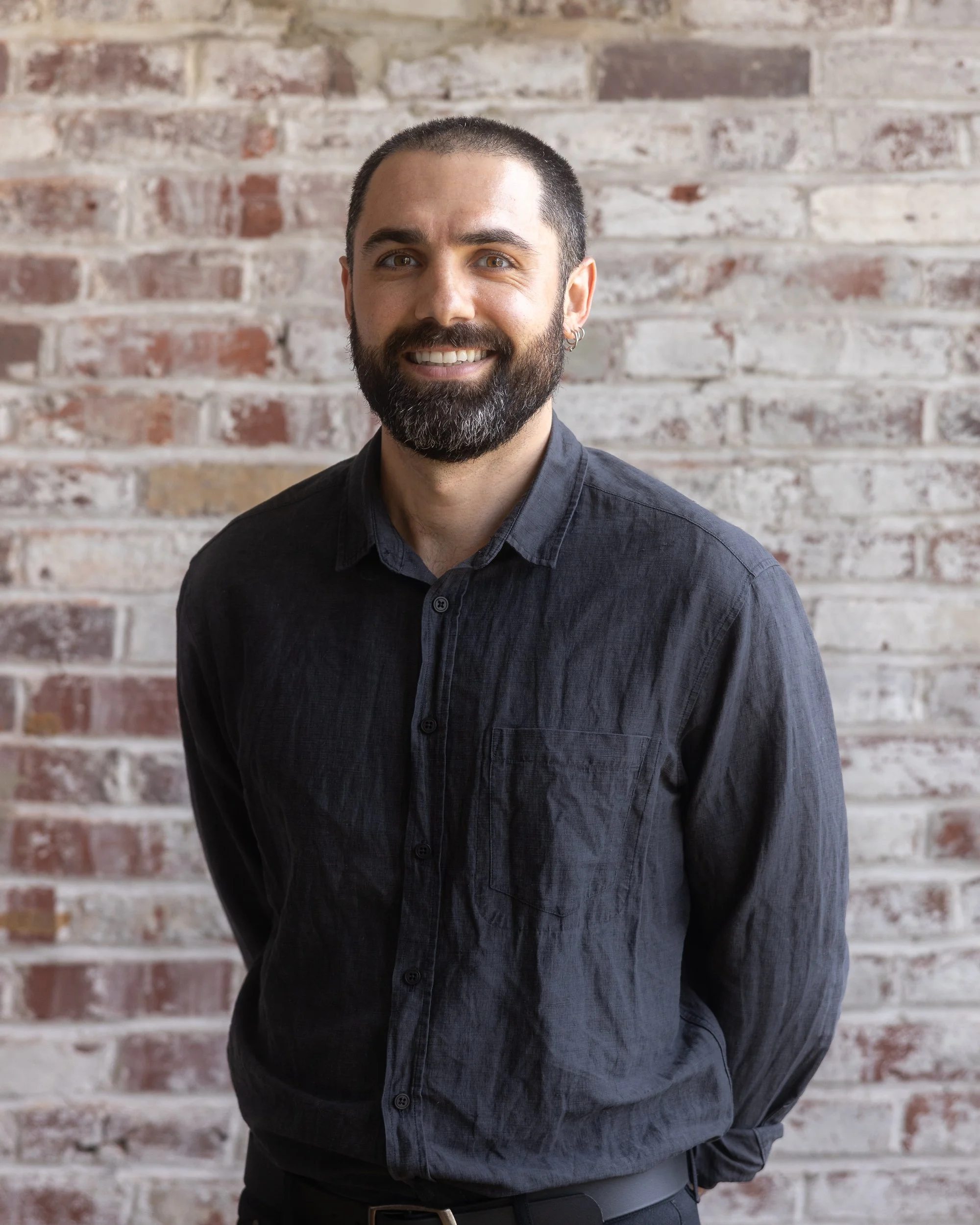 Photo of a man with a beard, smiling at the camera, wearing a dark button-up shirt.