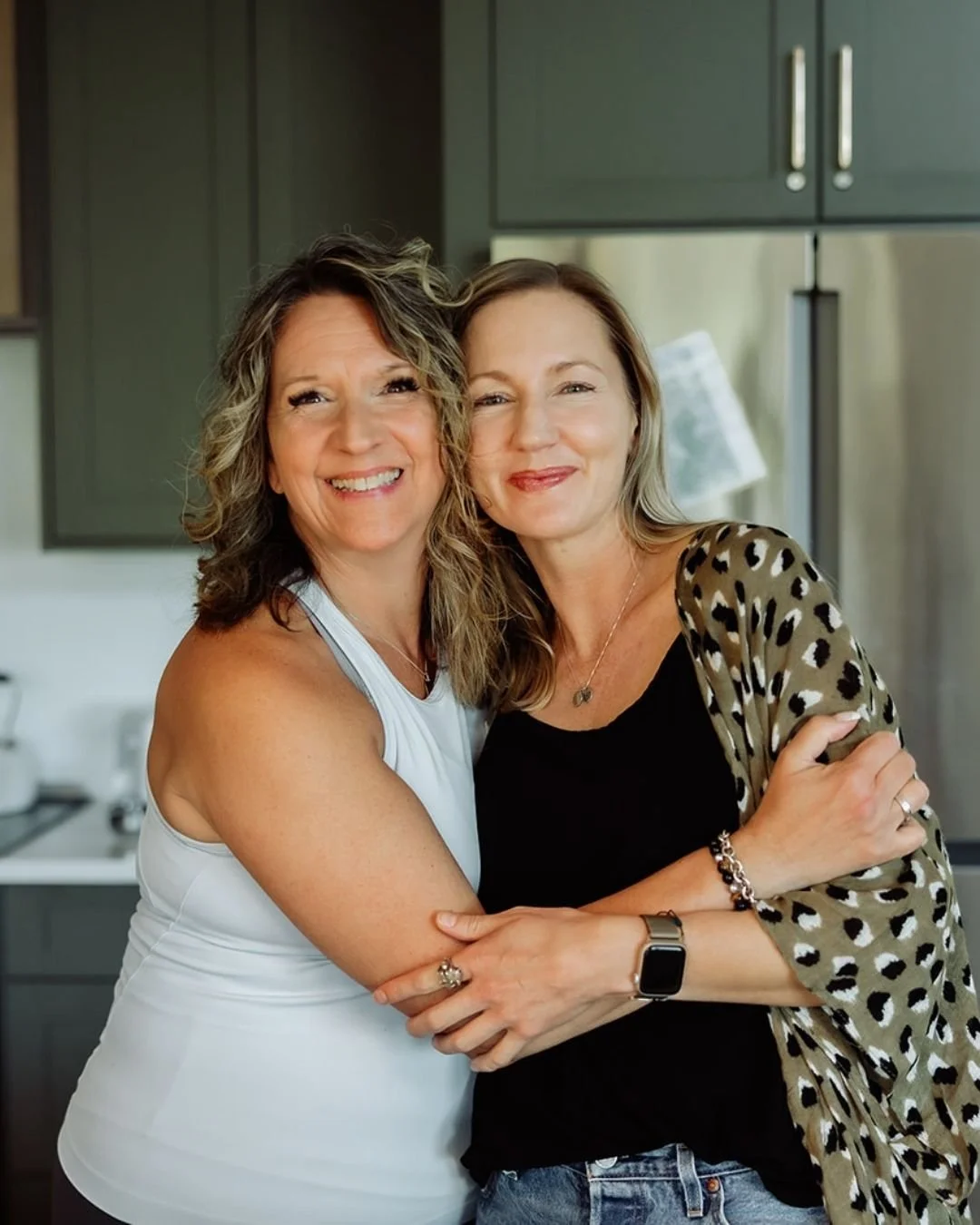 Two women embracing and smiling in a kitchen.