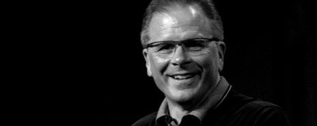 A smiling man with glasses in a dark environment.