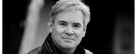 Black and white portrait of a man with light-colored hair and a slight smile, outdoors.