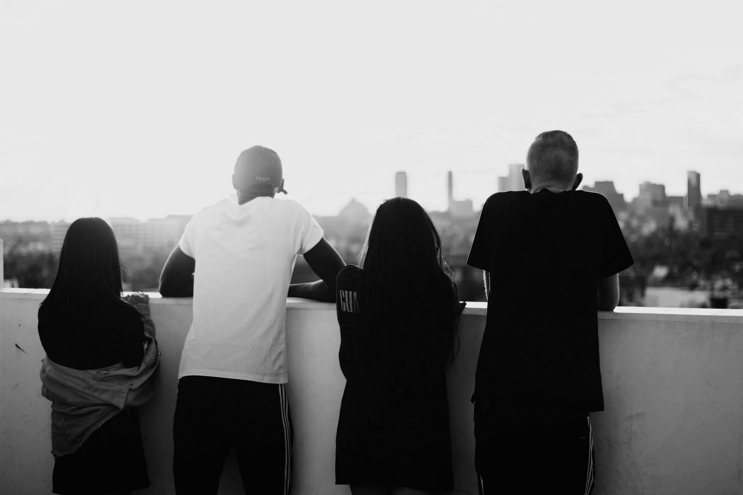 Four people standing on a rooftop observing a city skyline in the distance, in black and white.