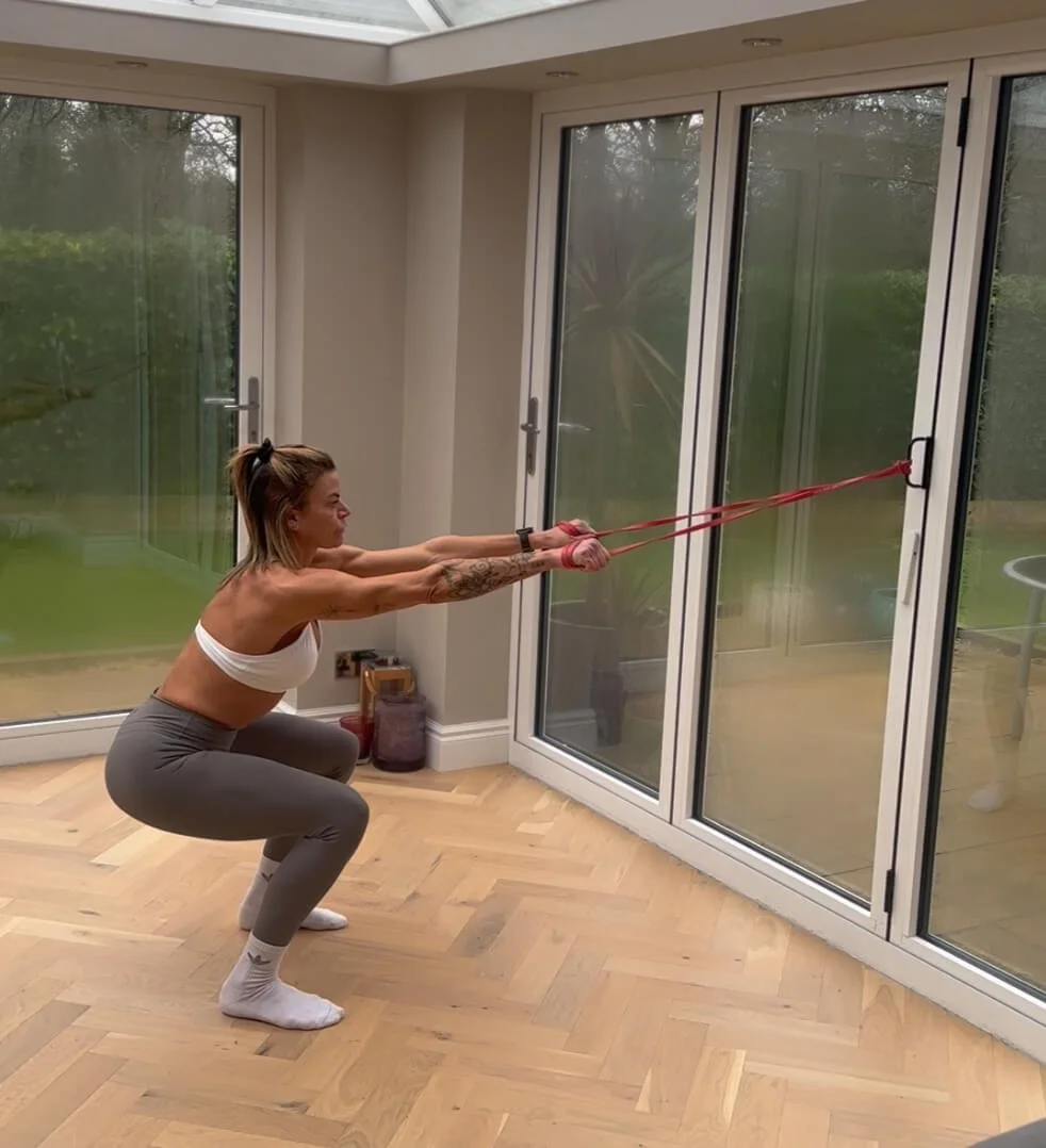 Claire doing a squat exercise using resistance bands anchored to the door handles using one of her home workouts from the app.