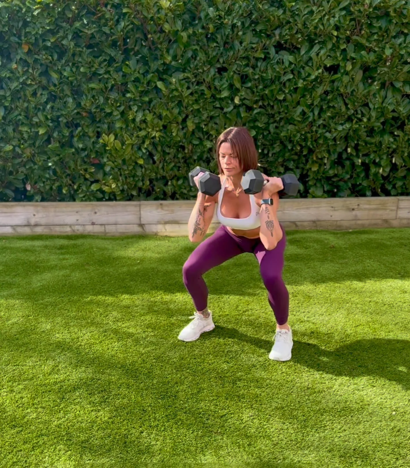 Claire is doing a dumbbell squat in the backgarden using one of her home workouts for women.