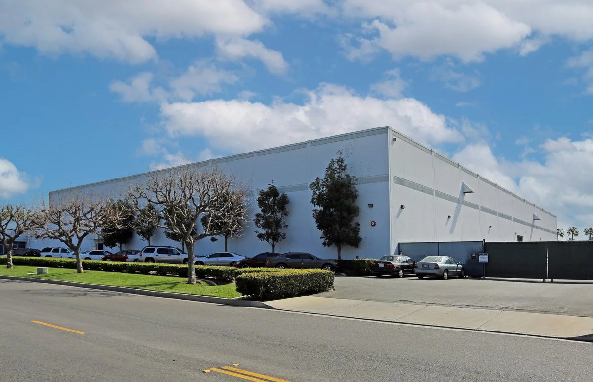 Industrial Building with blue sky and clouds and trees against it and a road
