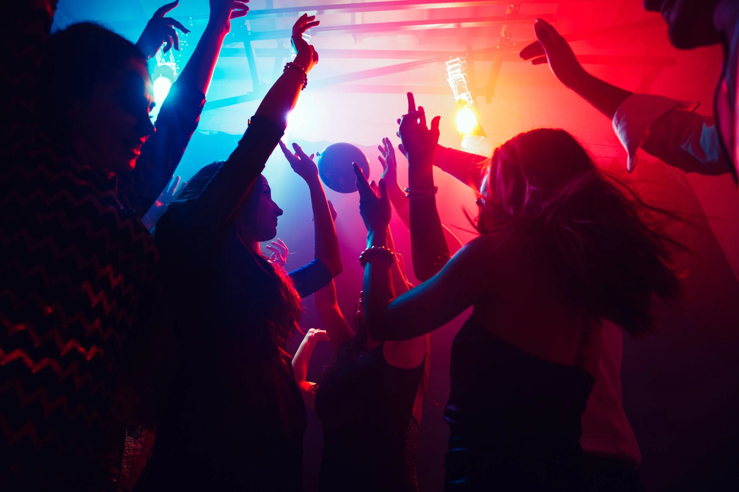 Women at a club dancing with their arms raised in the air