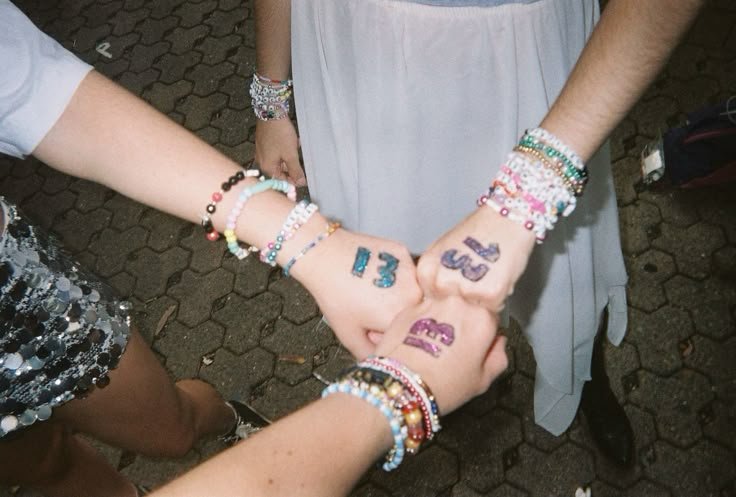Three fans at Taylor Swift's Eras Tour with friendship bracelets and the number 13 written on their hands